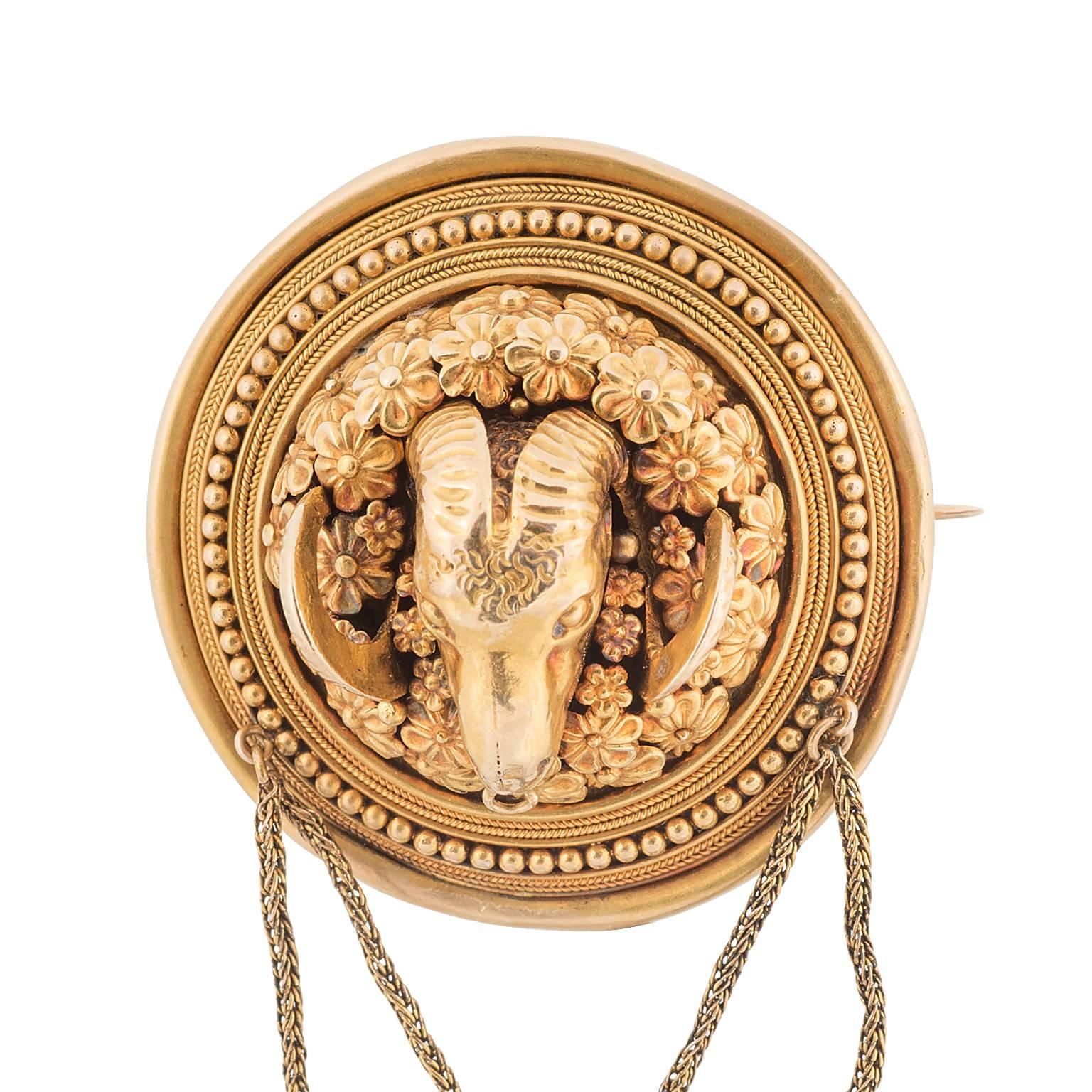 An Ernesto Pierret Victorian era 18 karat gold ram's head brooch.  The ram is magnificently handcrafted, surrounded by flowers, and enclosed in a circular frame with a combination of coin edge and beaded gold work.  The brooch features a glass