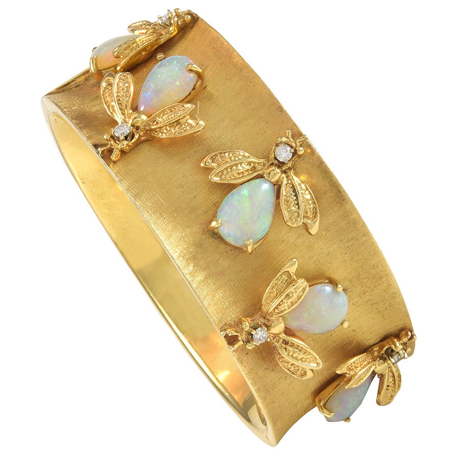 Pear shaped cabochon opal and round brilliant diamond bee bangle bracelet in 14k brushed yellow gold.  The bees rest on the top half of the bracelet only.