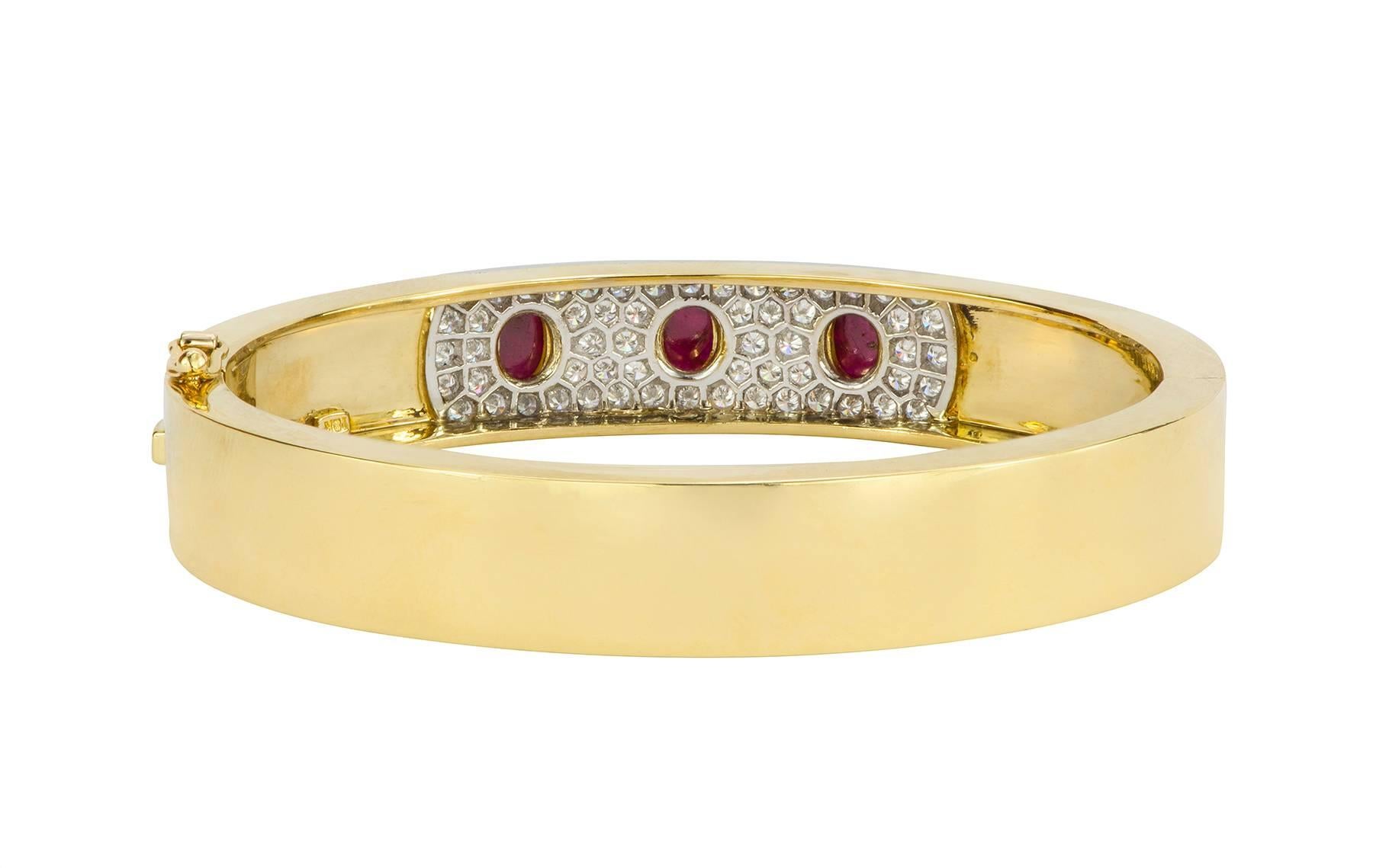 A hinged bangle bracelet made up of three cabochon rubies bezel set in a pave diamond station of platinum in the center of the 18k yellow gold bangle.  The three rubies have an estimated total weight of 2.30cts, with 0.82cts in diamonds.  The