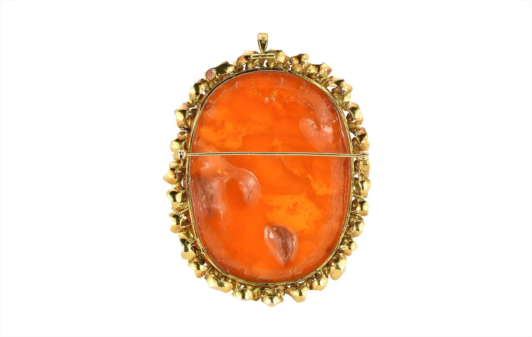 A large carved amber and 14k yellow gold pendant and brooch.  The carving depicts two peacocks with a floral background.  The amber is set with a textured double row frame in a foliate design.

Size:  3.55 in. x x 2.75 in.
Hallmark:  14K