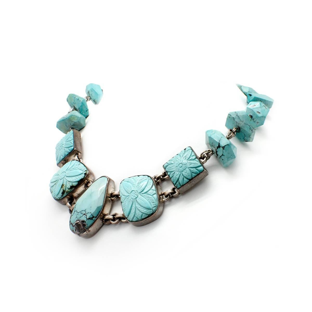 This one of a kind necklace is crafted with sterling silver by designer Stephen Dweck. The necklace is designed with bezel set turquoise carved with floral designs, as well as faceted turquoise pieces throughout. The necklace measures 40mm at its