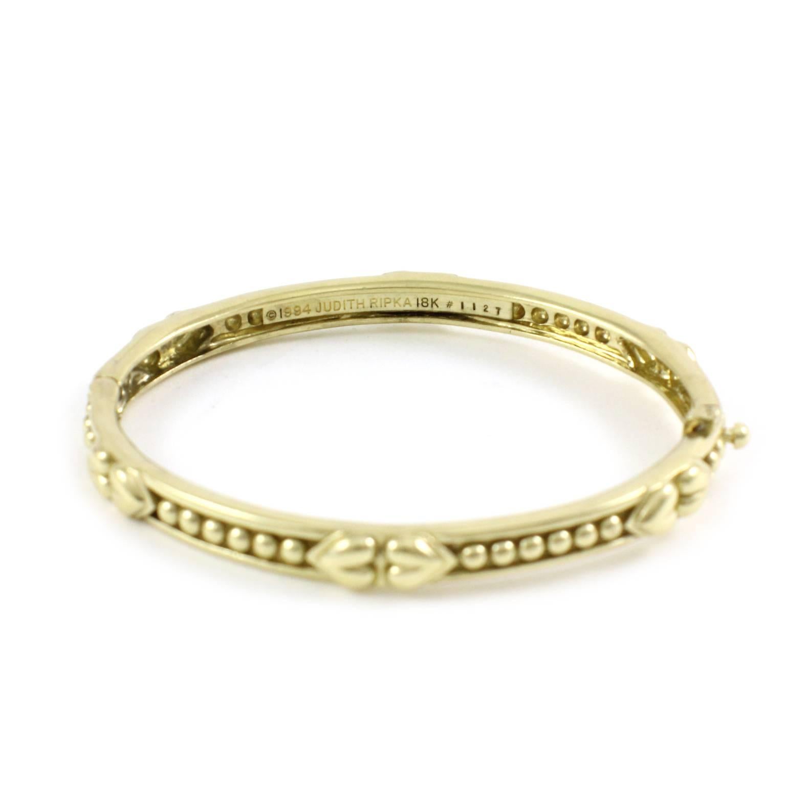 This bangle bracelet is made in 18k yellow gold by Judith Ripka. It is adorned with hearts. The bracelet measures 6mm wide, and it weighs 27.90 grams. The bracelet will fit up to a 6.5-inch wrist. 

The bracelet is signed 