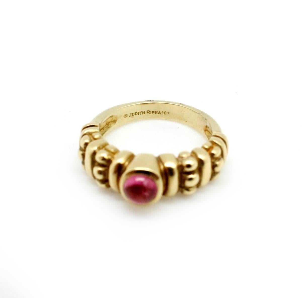 This ring is made in 18k yellow gold by Judith Ripka. The ring holds a single pink tourmaline cabochon at its center for vibrant color. The piece measures 7mm wide, and it weighs 9.1 grams. The ring is a size 7, and it is signed 