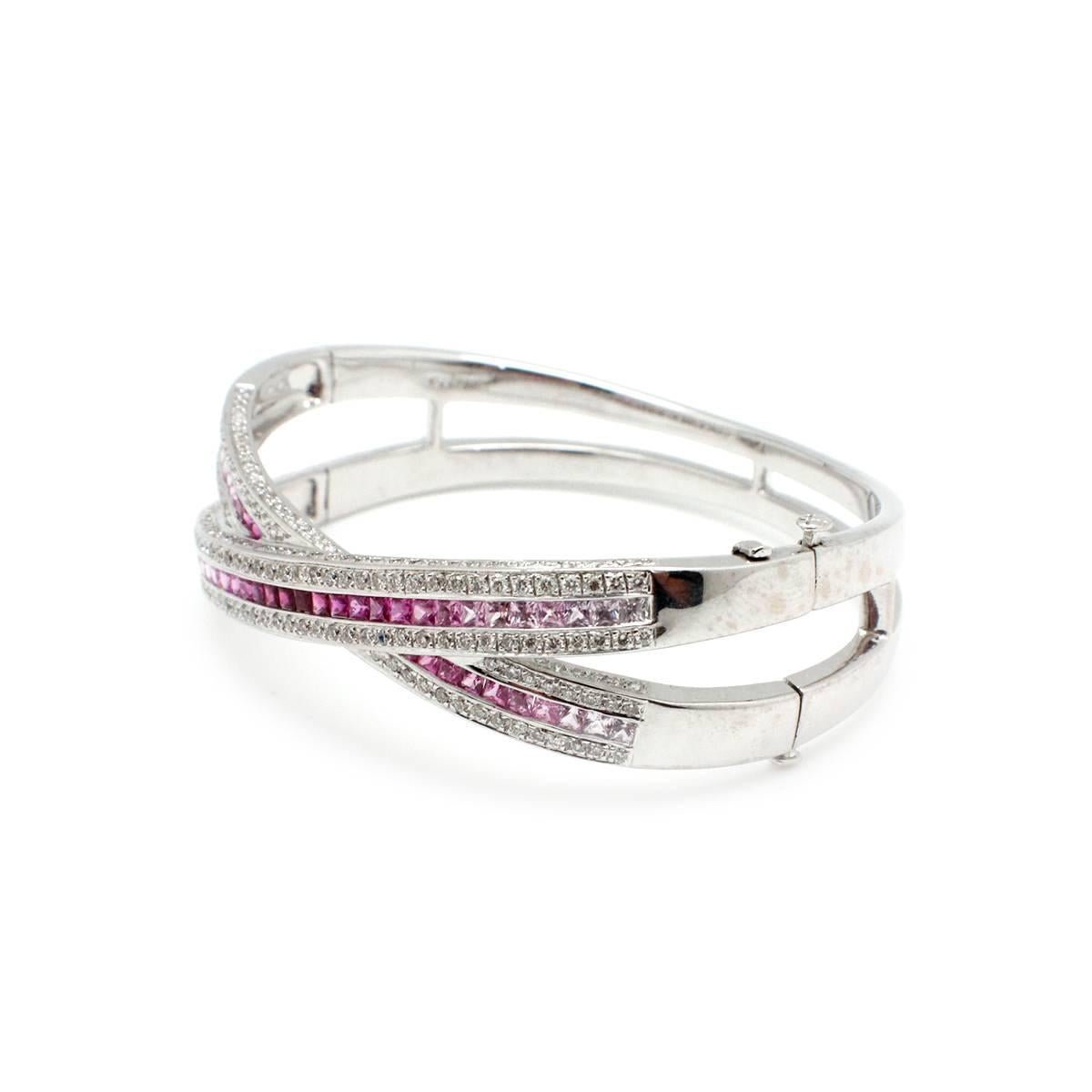 This unique bangle bracelet is crafted in 18k white gold. Precious pink sapphires and are given luxurious direction with this crossover bangle bracelet design. 18k white gold steers the diamonds and pink sapphires, creating a captivating rhythm for