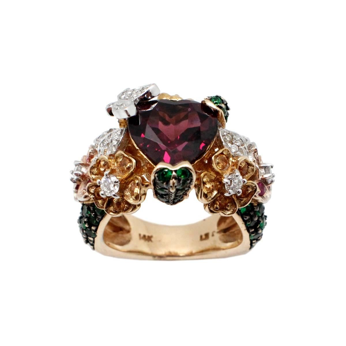 This ring is stunning! It is made in both 14k yellow and 14k white gold. The ring features a large heart-cut pyrope garnet at its center, and that stone is accented by other vibrant gemstones. The gemstones include 23 round brilliant diamonds, 66