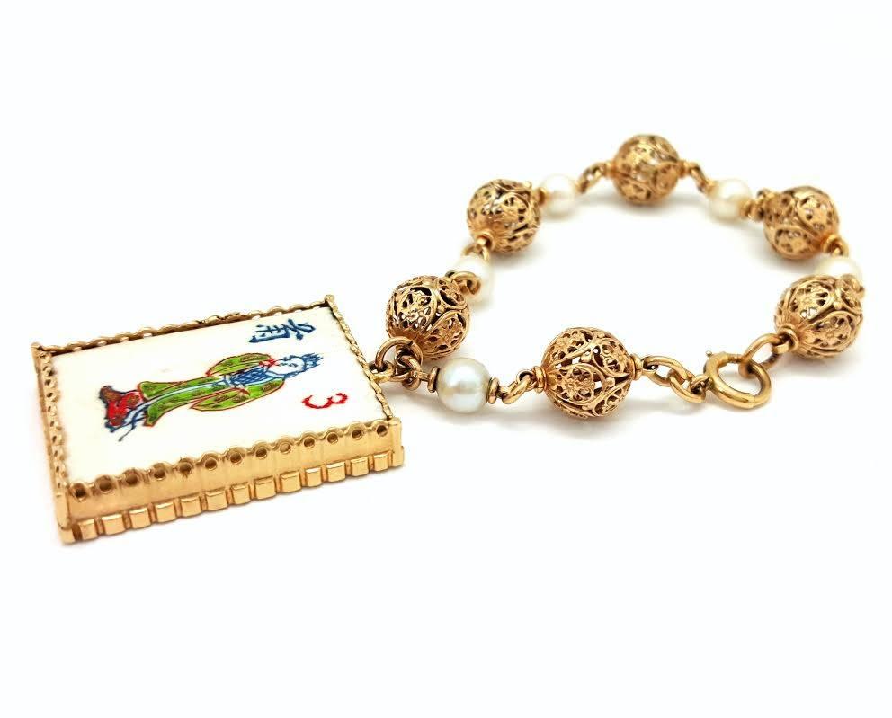 This unique bracelet is made in 14k yellow gold with pearl accents. The pearls measure about 6mm in diameter, and the chain measures 10mm wide. The bracelet has a single charm which is a Mahjong tile set into 14k yellow gold. The charm measures
