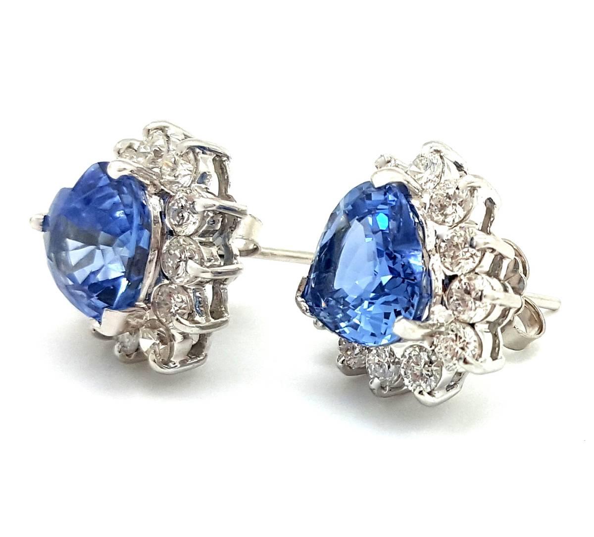 These gorgeous earrings will make your heart sing! The earrings are made in 18k white gold. Each lovely earring features a heart shaped Ceylon cornflower colored blue sapphire set with a halo of 12 round diamond melee. These beautiful diamonds have