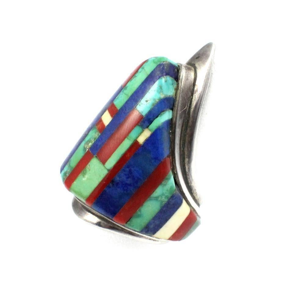 This beautiful sterling silver Hopi shield ring was designed by world renowned American Indian artist Charles Loloma. The ring is cast in sterling silver and consists of turquoise, lapis, and coral inlay. The ring measures approximately 1.75-inches