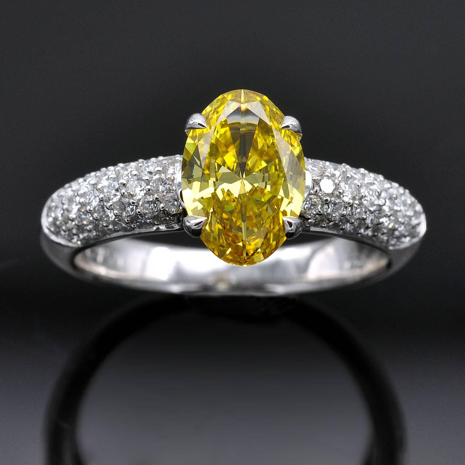 A very fine diamond engagement ring. Set in its center an oval fancy vivid yellow diamond weighing 1.36 cts. Its rich color is the most desirable : vivid in tone and hue (not deep or dark just vibrant). Its shape, an elegant oval very well cut: with