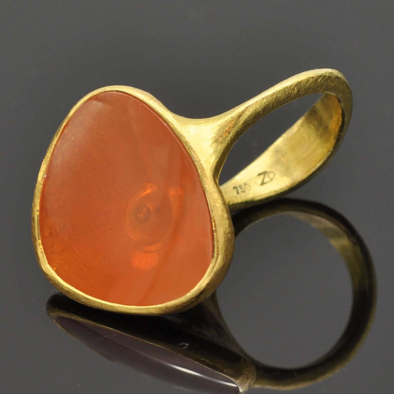 This unique modernist ring seems to get its ethnic inspiration from antique times. A besel set fire opal (16,67 carat ) and beneath it a diamond (0.06 ct) . The ring itself is 18 KT gold.  The opal is nested between two fingers thanks to The sensual