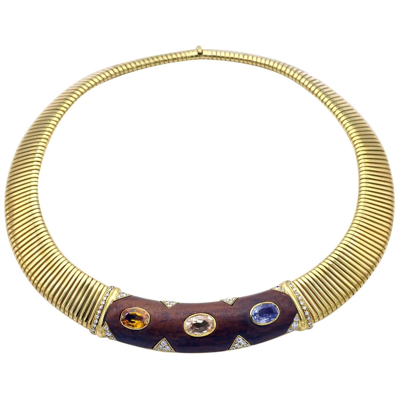 Iconic Gold tubogas necklace. the central element is inlayed with wood, in which a yellow sapphire a soft pink sapphire and a blue sapphire are set . Elegantly placed white diamonds highlight the whole necklace. This choker is excessively well made