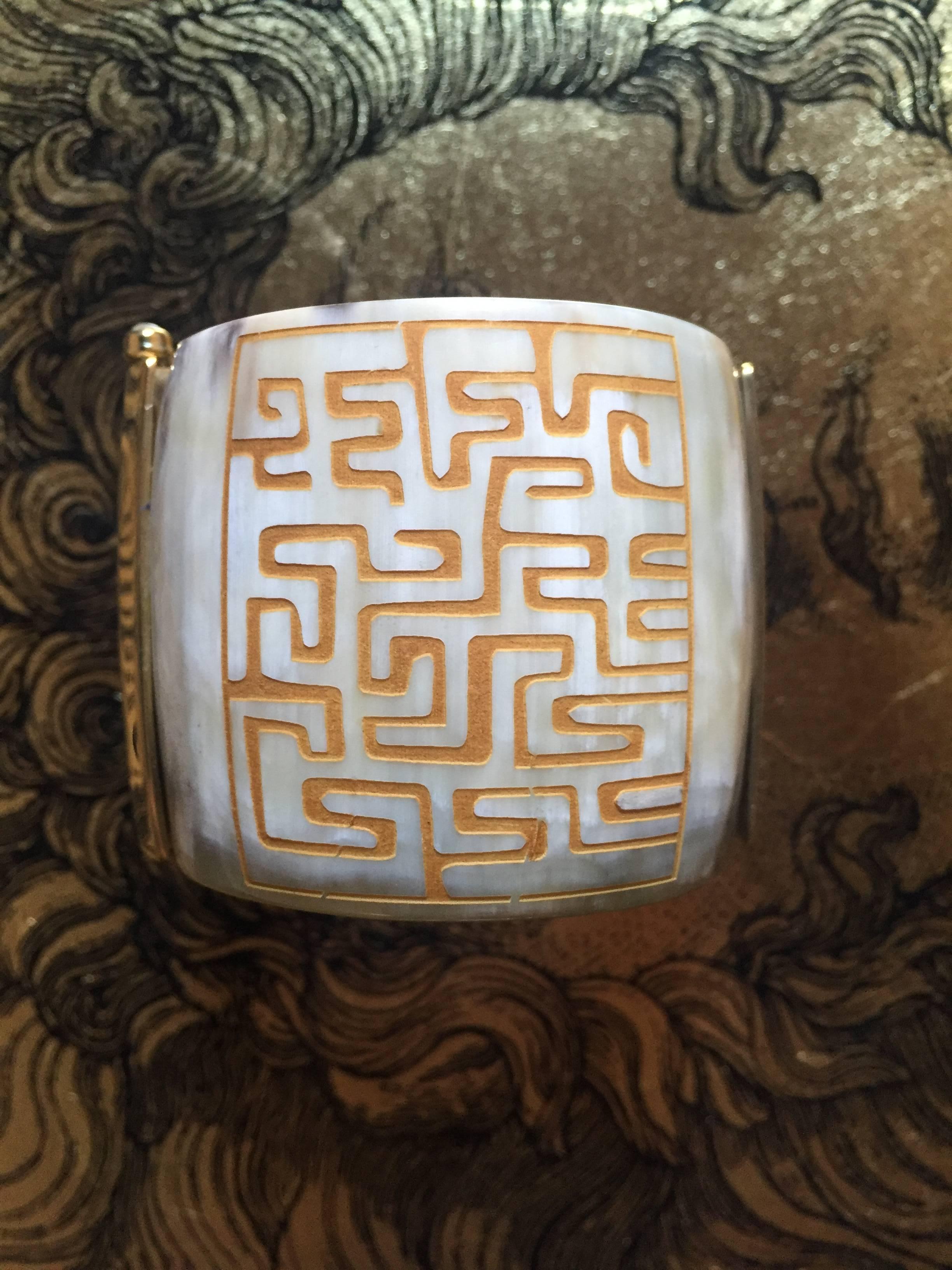 This unique cuff is crafted from African cow horn and engraved with a geometric motif on one side; the other side is not engraved;  showing the natural marbled graining of cow horn. The intricate pin-clasp is set with a  fire-opal sourced from