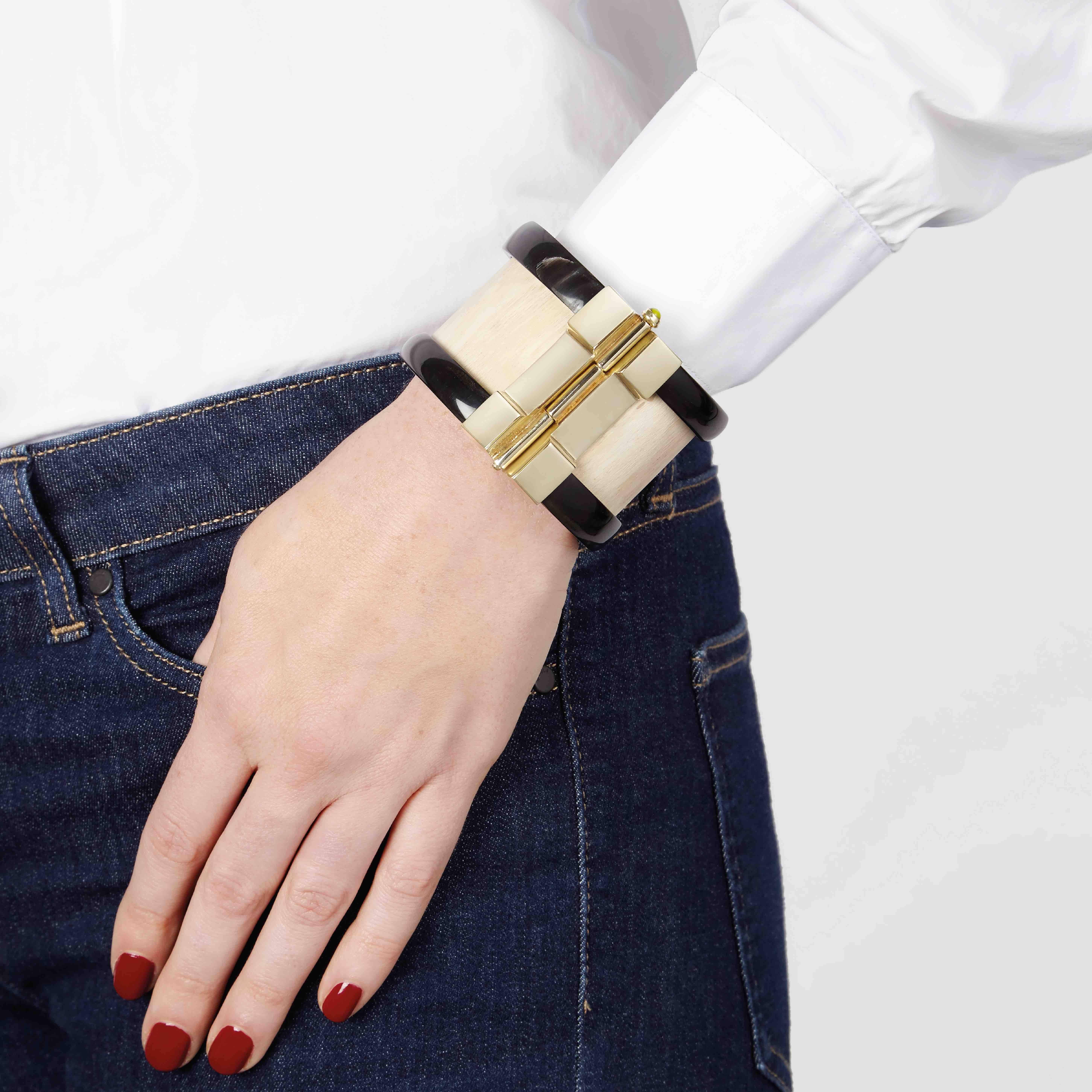 Cuff bracelet crafted by hand from jacaranda wood and African cow horn. The customizable 18k gold plated pin-clasp is set with choice or green peridot, ruby or emerald. Inspired by warrior style cuffs worn by former Vogue editor Diana Vreeland.