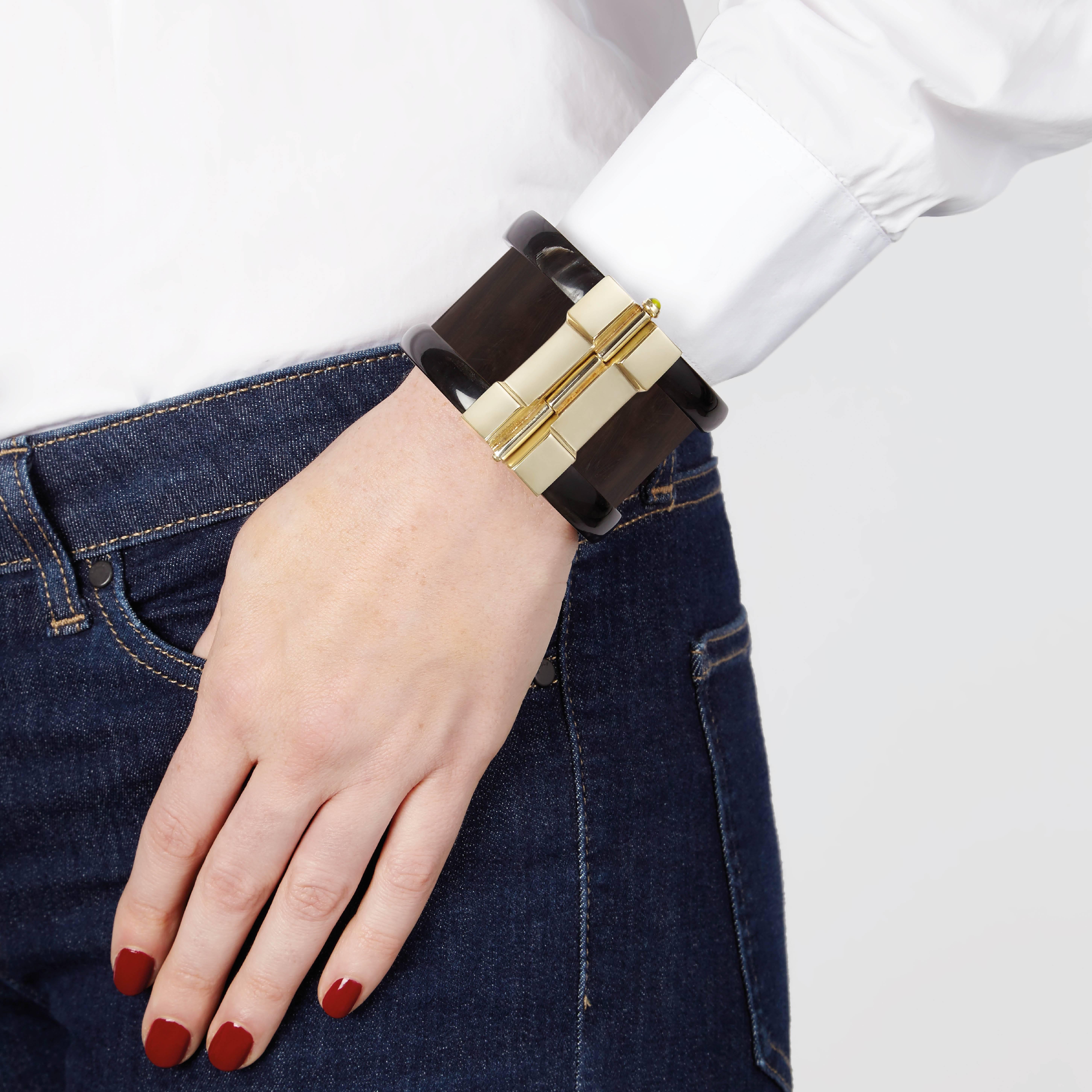 Cuff bracelet hand crafted from ebony wood and African cow horn. The customizable 18k gold plate pin-clasp is set with a choice of ruby, sapphire or emerald. Inspired by warrior style cuffs worn by former Vogue editor Diana Vreeland. 

Each cuff is