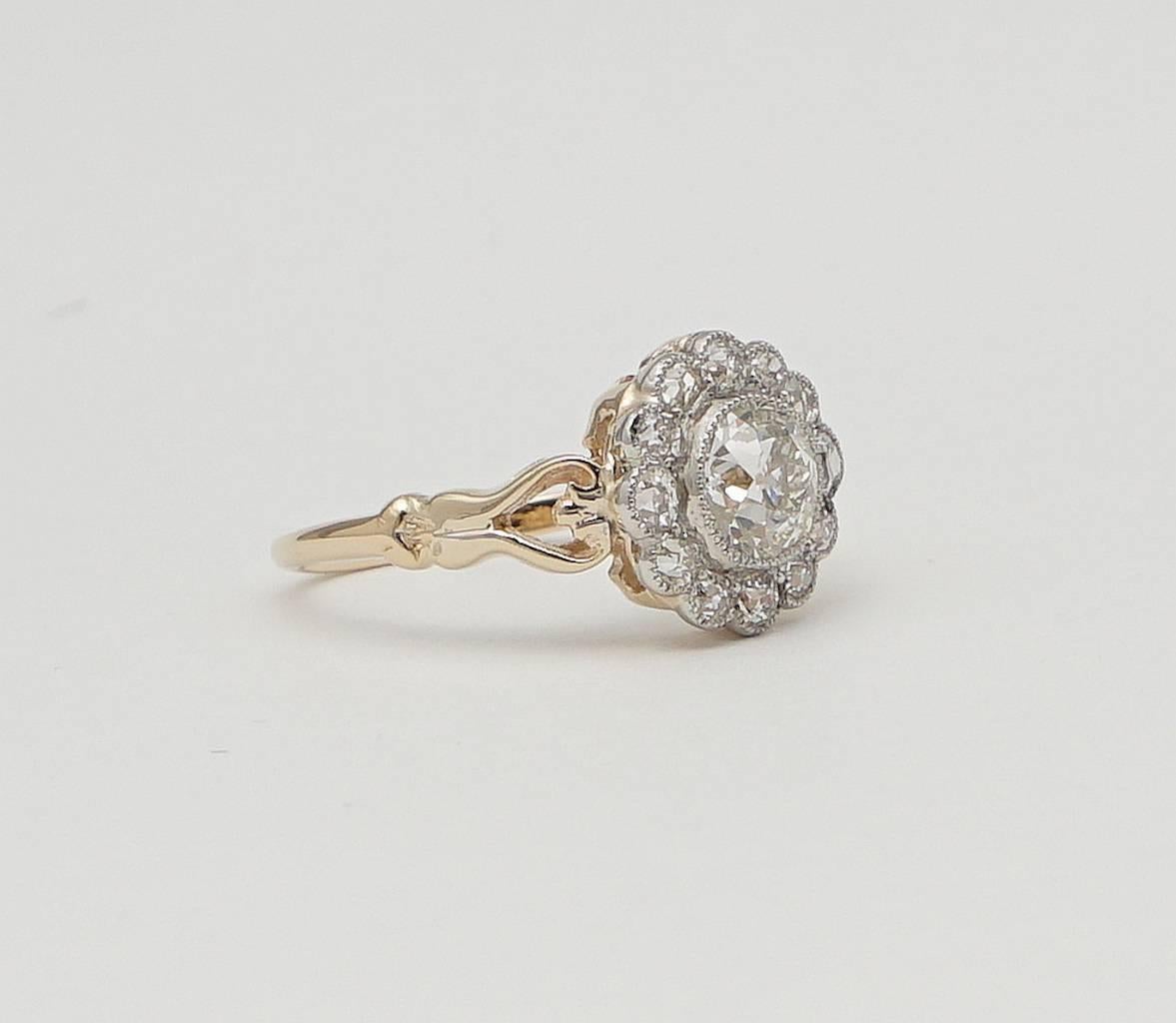 A beautiful original edwardian period diamond engagement ring in luxurious platinum and 18 karat yellow gold. Centered by a sparkling antique old European cut diamond surrounded by a dozen accenting old European cut diamonds this ring features a