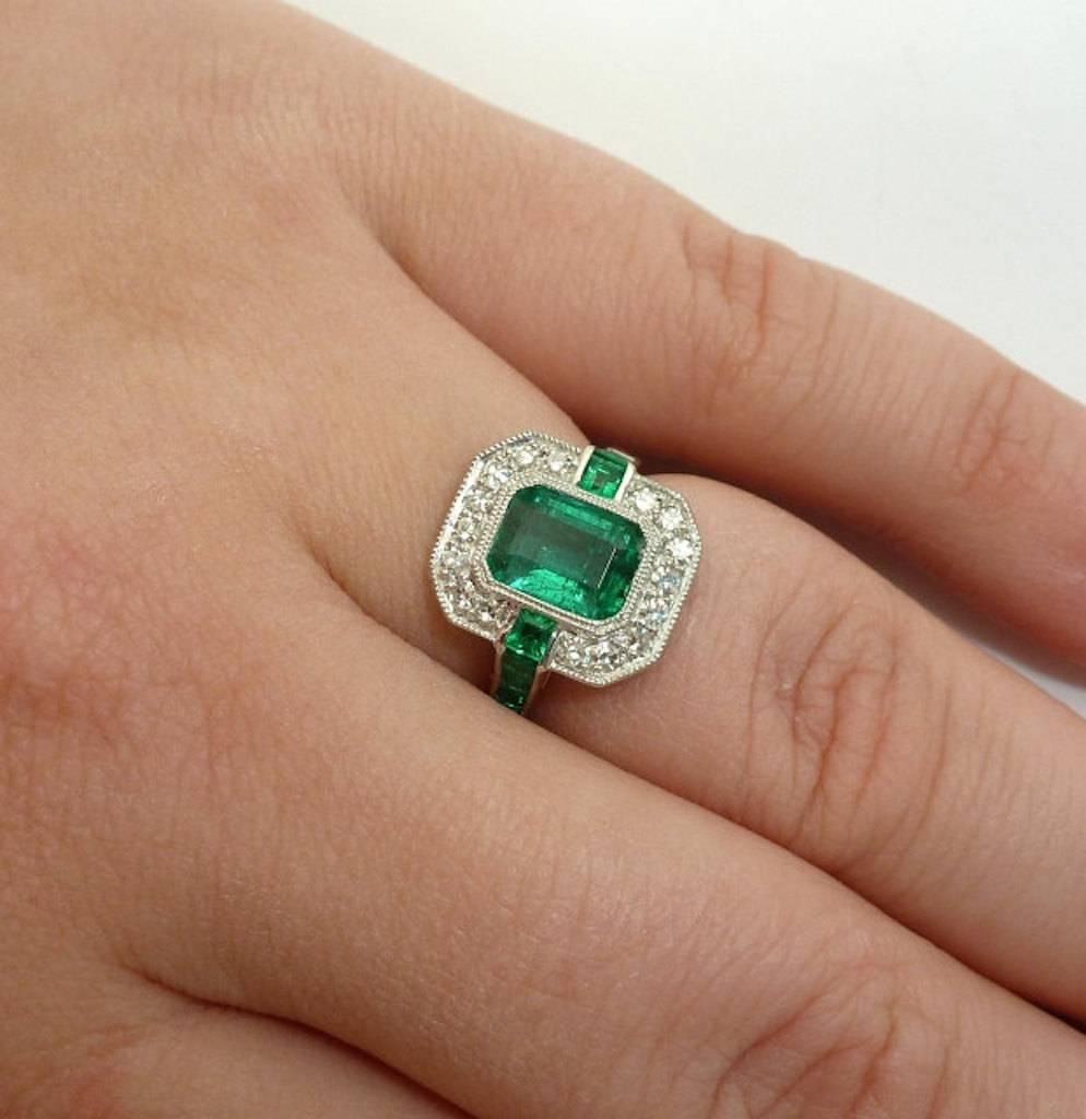 A stunning modern British emerald and diamond ring in luxurious 900 fine platinum. Centered by a substantial 1.84 carat Colombian emerald, this beautiful ring features channel set calibre cut emeralds, sparkling single cut diamonds, and hand applied