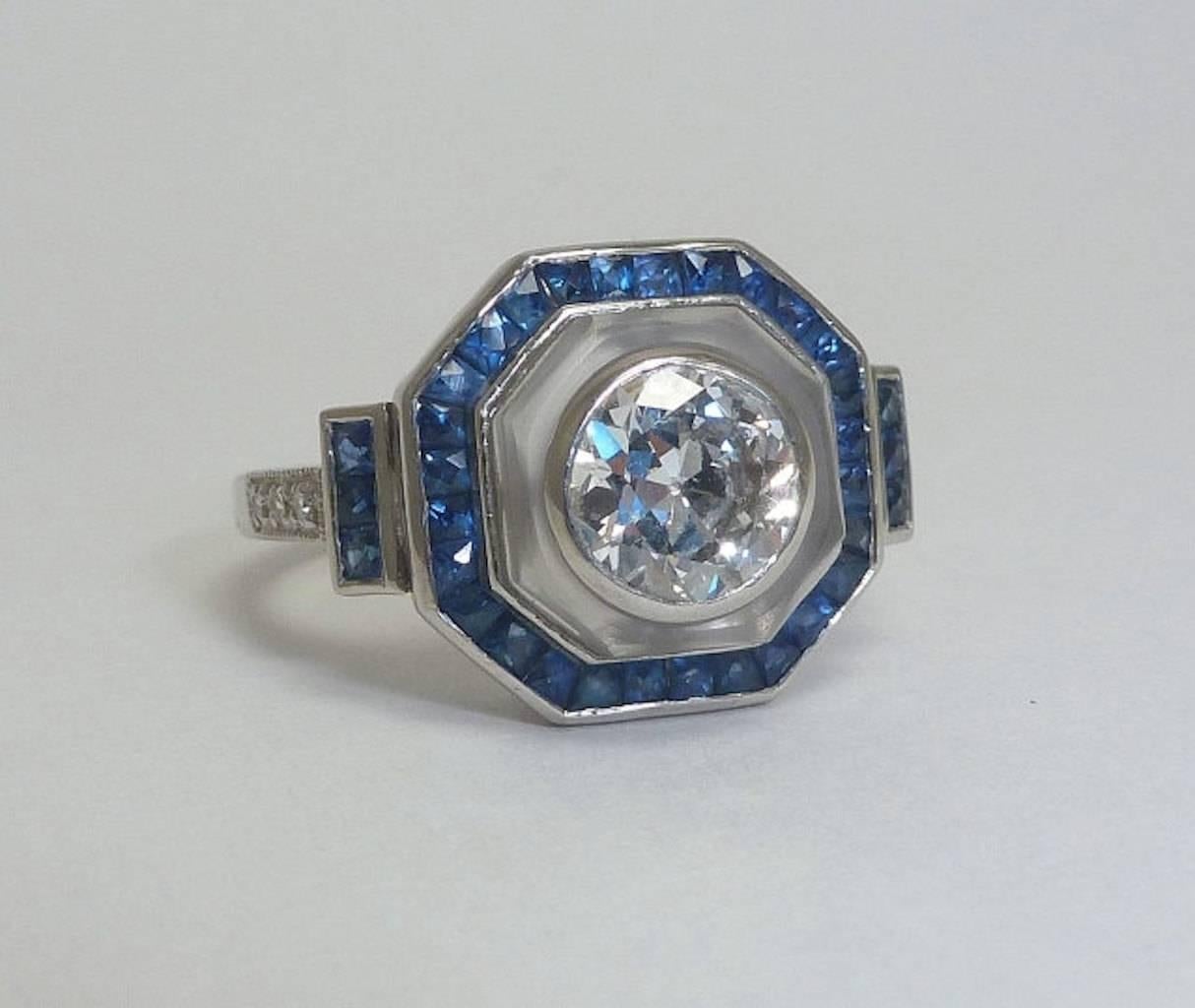 A beautiful sapphire and diamond engagement ring in luxurious platinum. Featuring a center bezel set old European cut diamond framed by frosted rock crystal and French cut sapphires this ring is truly a spectacular and unique engagement ring of the