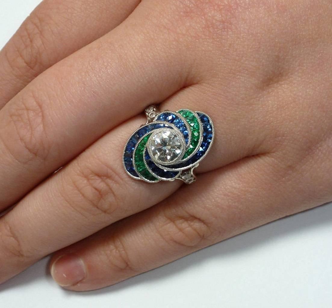 An absolutely incredible diamond, emerald, and sapphire ring in platinum. A true show stopper, this amazing ring is centered by a gorgeous 1.20 carat diamond surrounded by masterfully French cut emeralds and sapphires in a stunning hand crafted