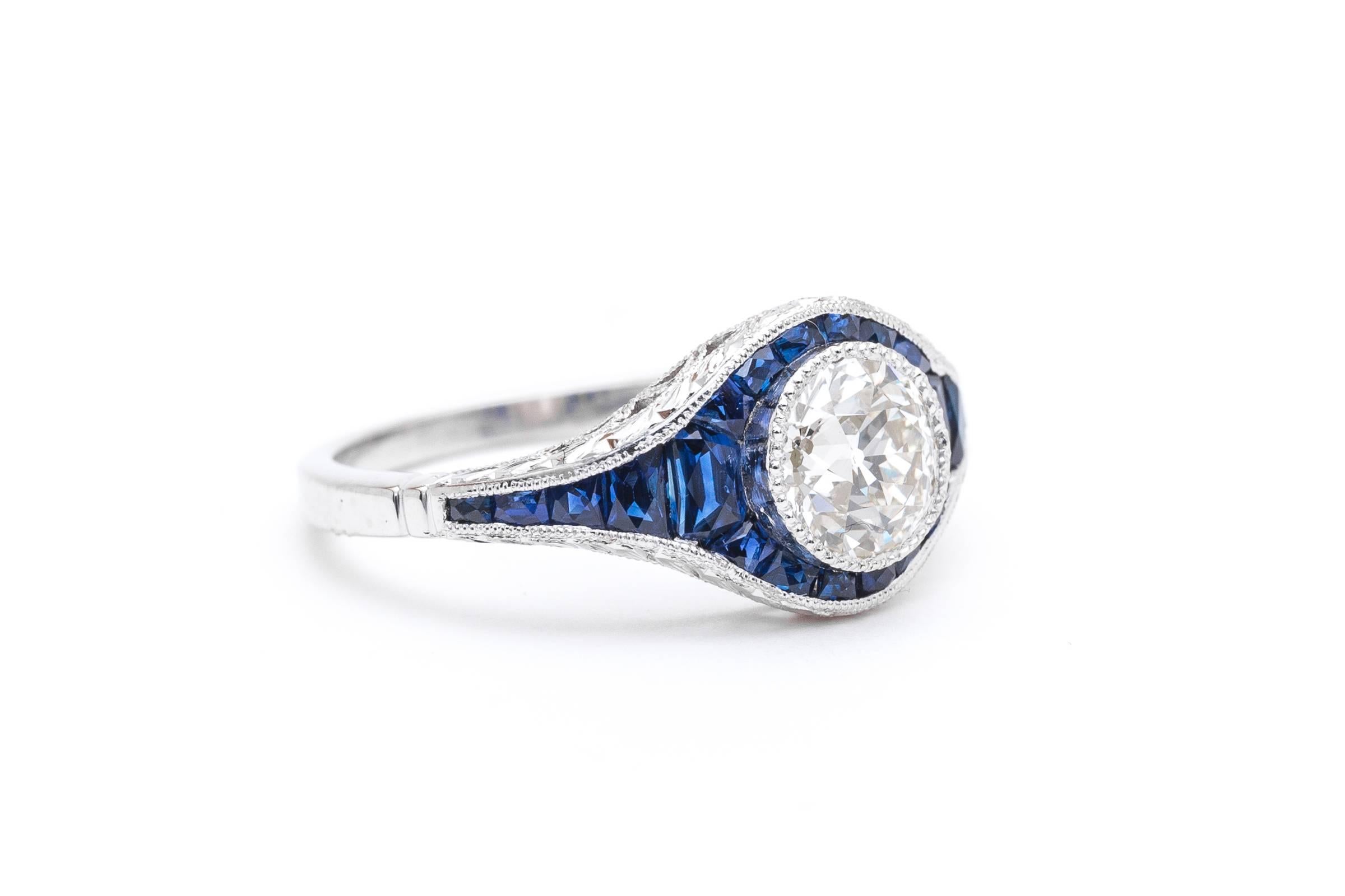 A stunning diamond, and French cut sapphire engagement ring in luxurious platinum. Centered by a 1.10 carat antique European cut diamond this ring features a center bezel set diamond framed by beautiful rich vivid blue French cut sapphires in a hand