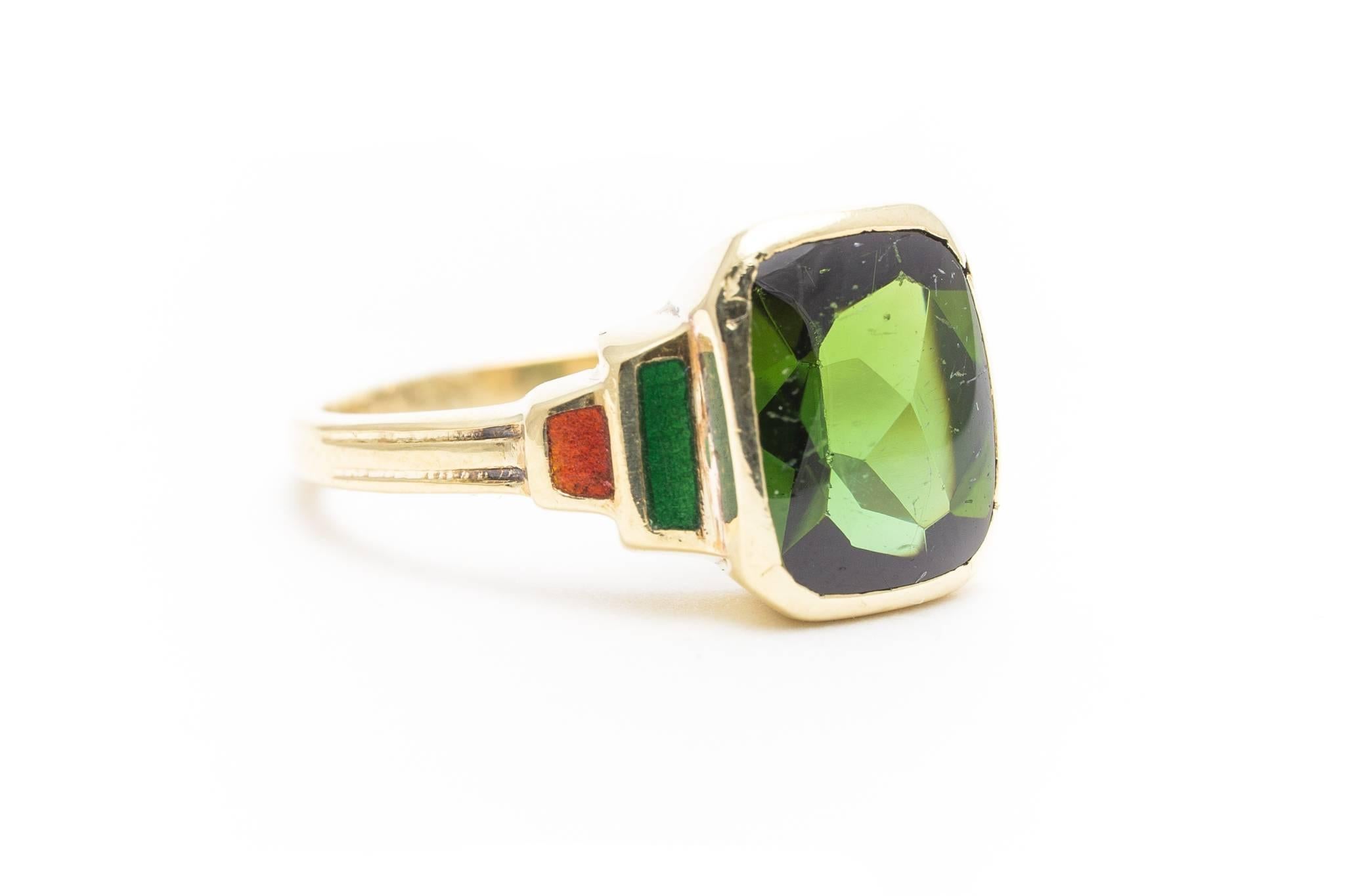 An original art deco period tourmaline and enamel ring in 14 karat yellow gold. Centering this ring is a rectangular cabochon cut green tourmaline weighing approximately 4 carats. Framing the center tourmaline, is beautiful richly colored red and