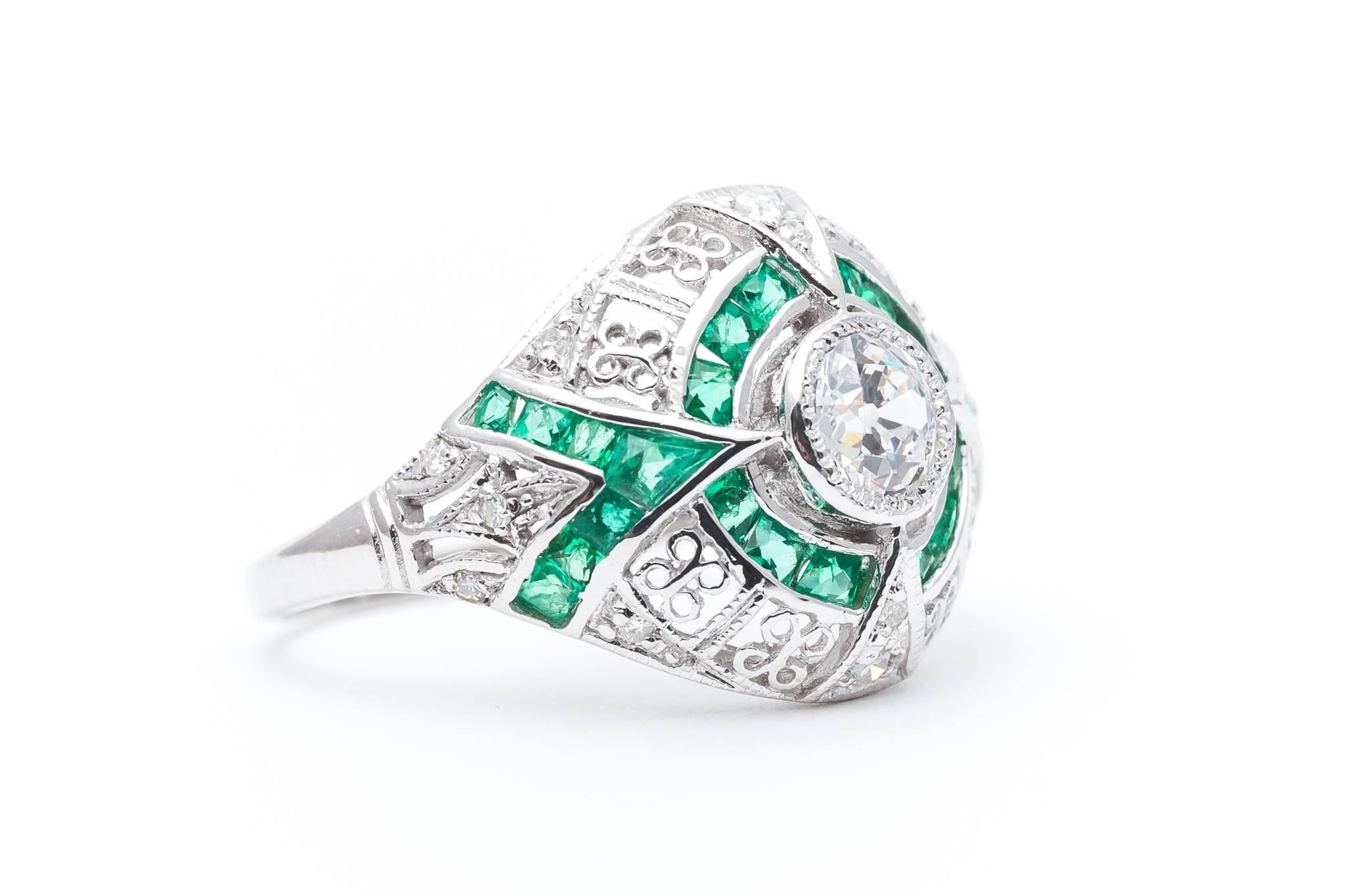 A stunning emerald and diamond engagement ring in 14 karat white gold. Centered by a sparkling antique European cut diamond of 0.60 carats, this stunning ring is set throughout with hand French cut emeralds, and sparkling antique cut diamonds all in
