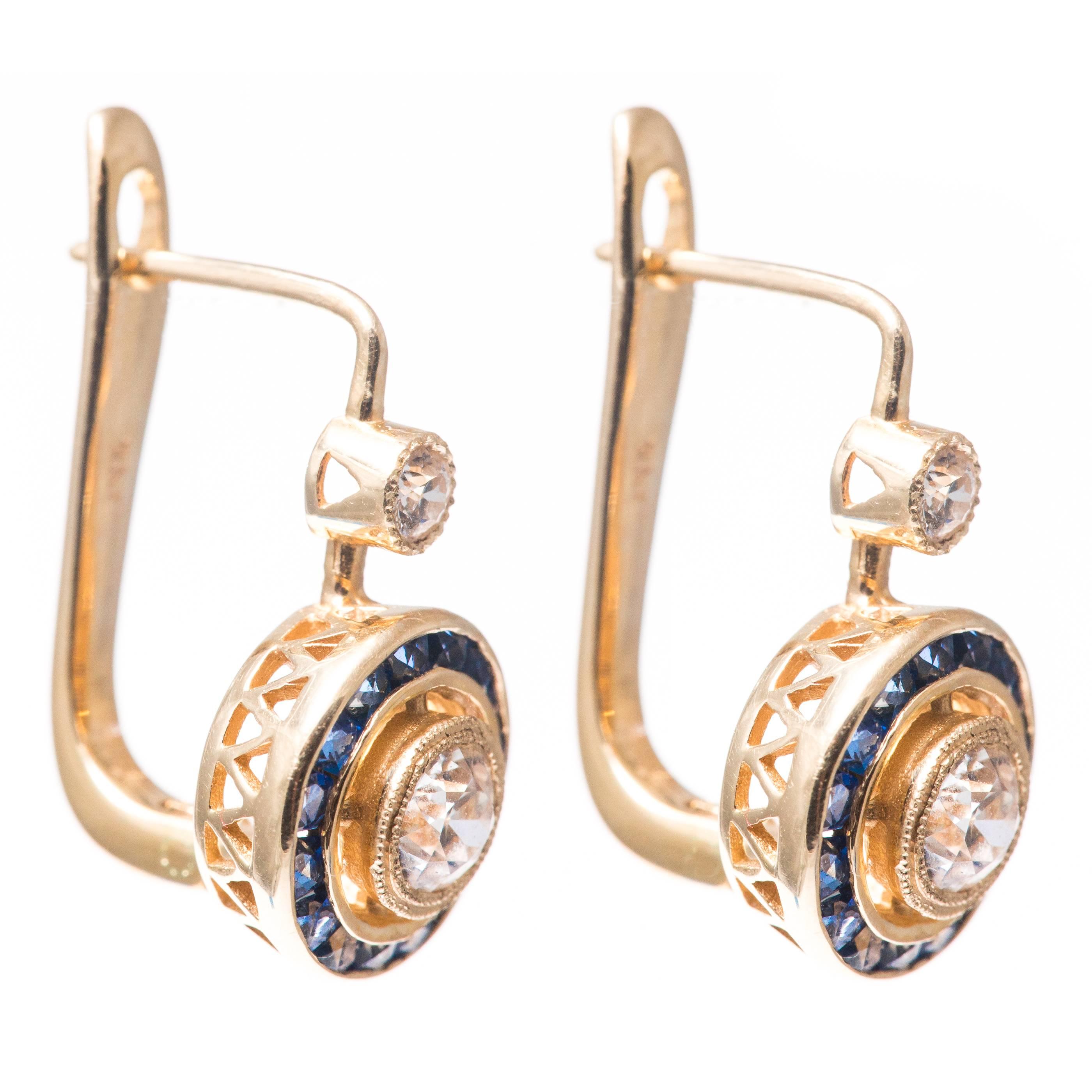 A pair of beautiful target style diamond and sapphire earrings in 14 karat yellow gold. Centered by a pair of old European cut diamonds these diamonds feature halos of French cut vivid blue sapphires surrounding the sparkling diamonds.  

Grading as