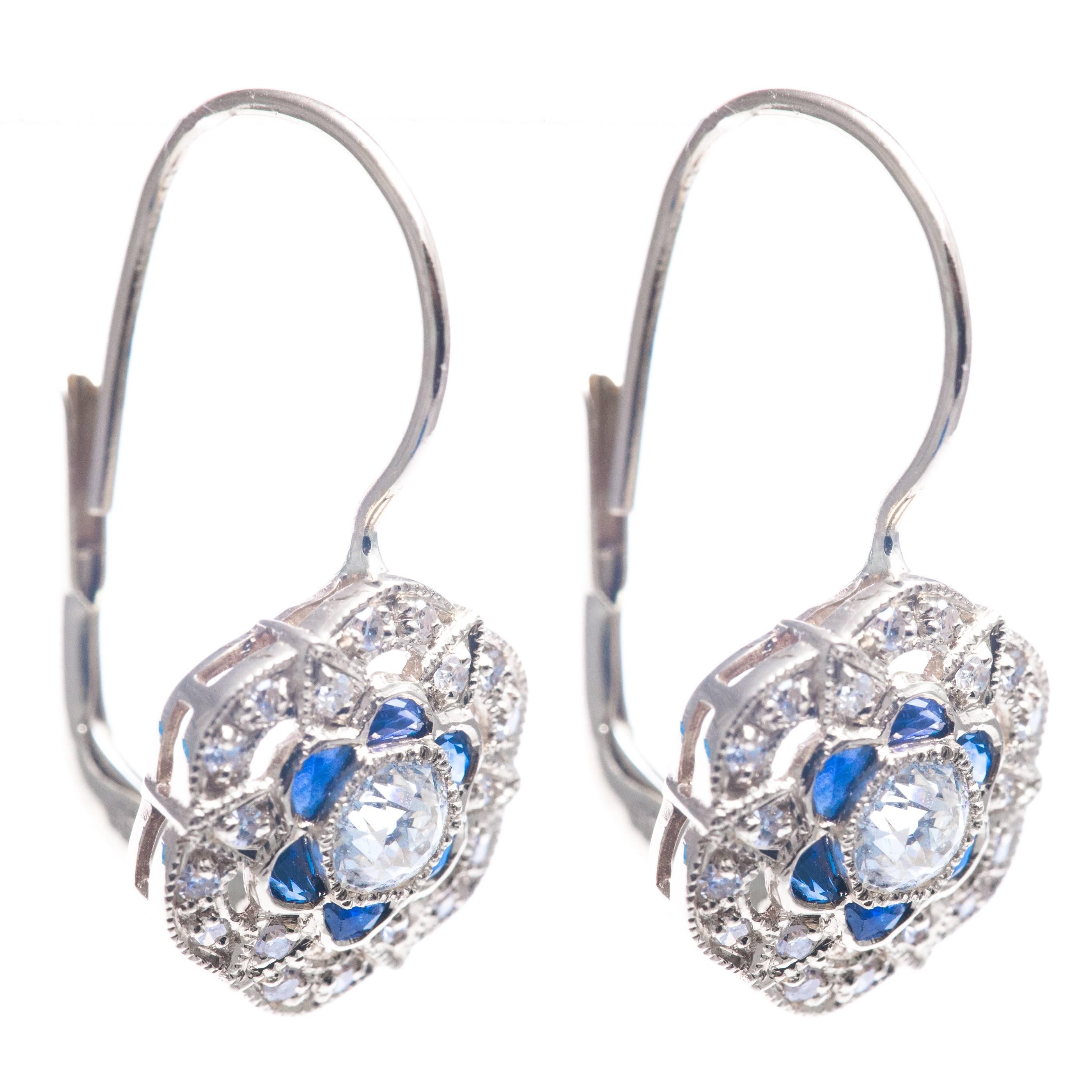 A beautiful pair of diamond and sapphire flower motif earrings in 14 karat white gold.  Centered by bezel set antique European cut diamond these earrings feature bespoke sapphire petals and are accented by a plethora of pave set diamonds.

Of