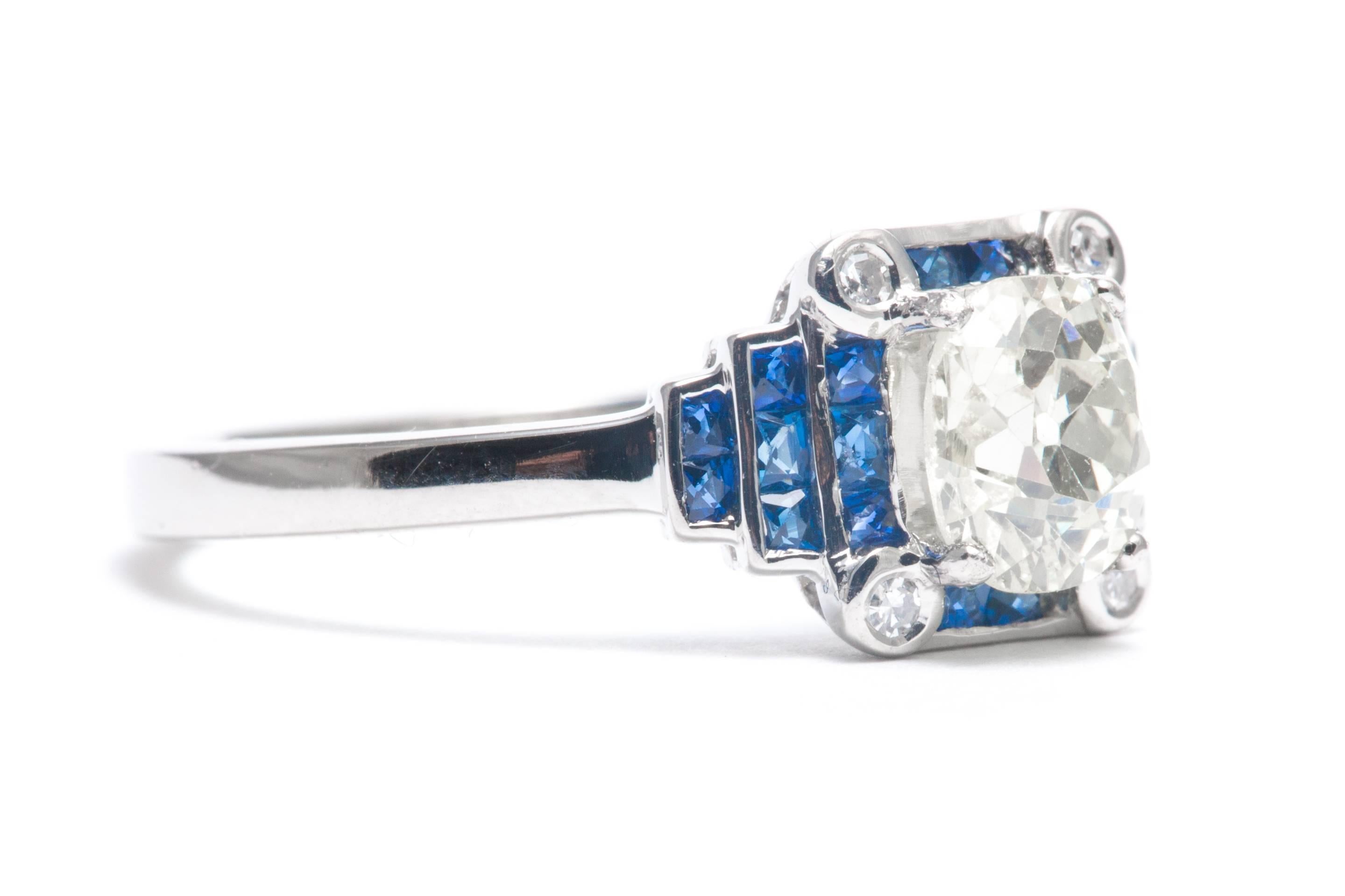 A beautiful stepped design diamond and sapphire engagement ring in luxurious platinum.  Centered by a 1.05 carat antique European cut cushion shaped diamond, this ring features a border of rich vivid blue French cut sapphires surrounding the center