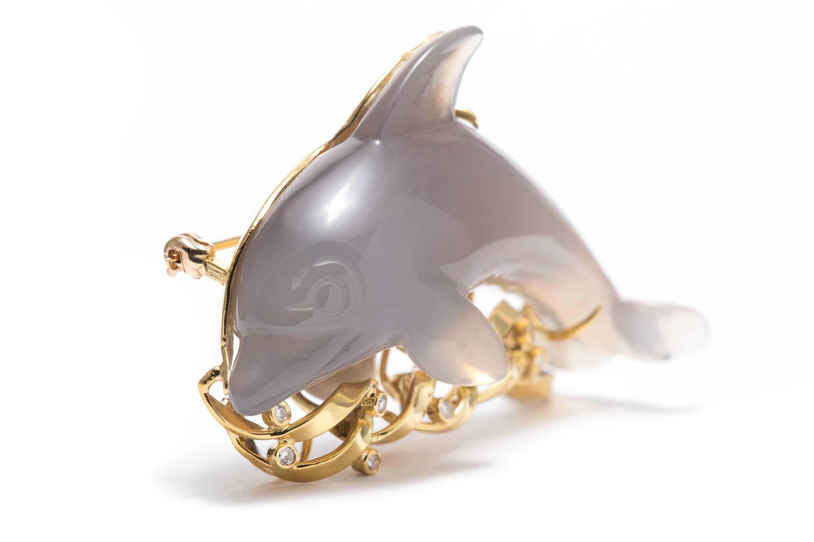 A stunning diamond set brooch designed as a carved chalcedony dolphin atop 18 karat yellow gold and diamond set waves.

Beautifully hand carved in chalcedony, the dolphin is depicted swimming over a sea of 18 karat yellow gold.  Embellished with