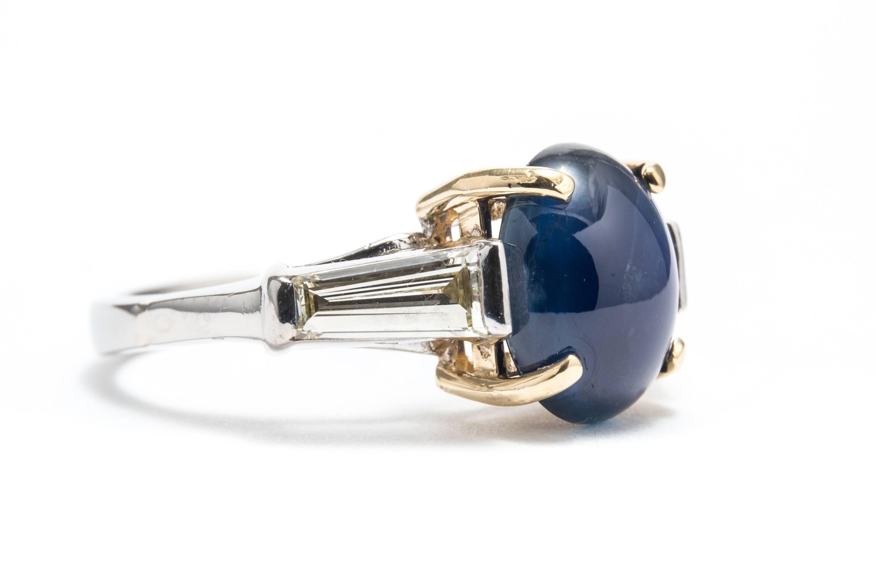A beautiful sapphire, and baguette diamond ring in luxurious platinum and 18 karat yellow gold.  Centered by a rich vivid blue cabochon sapphire, this ring also features a pair of sparkling tapered baguette cut diamonds framing the
