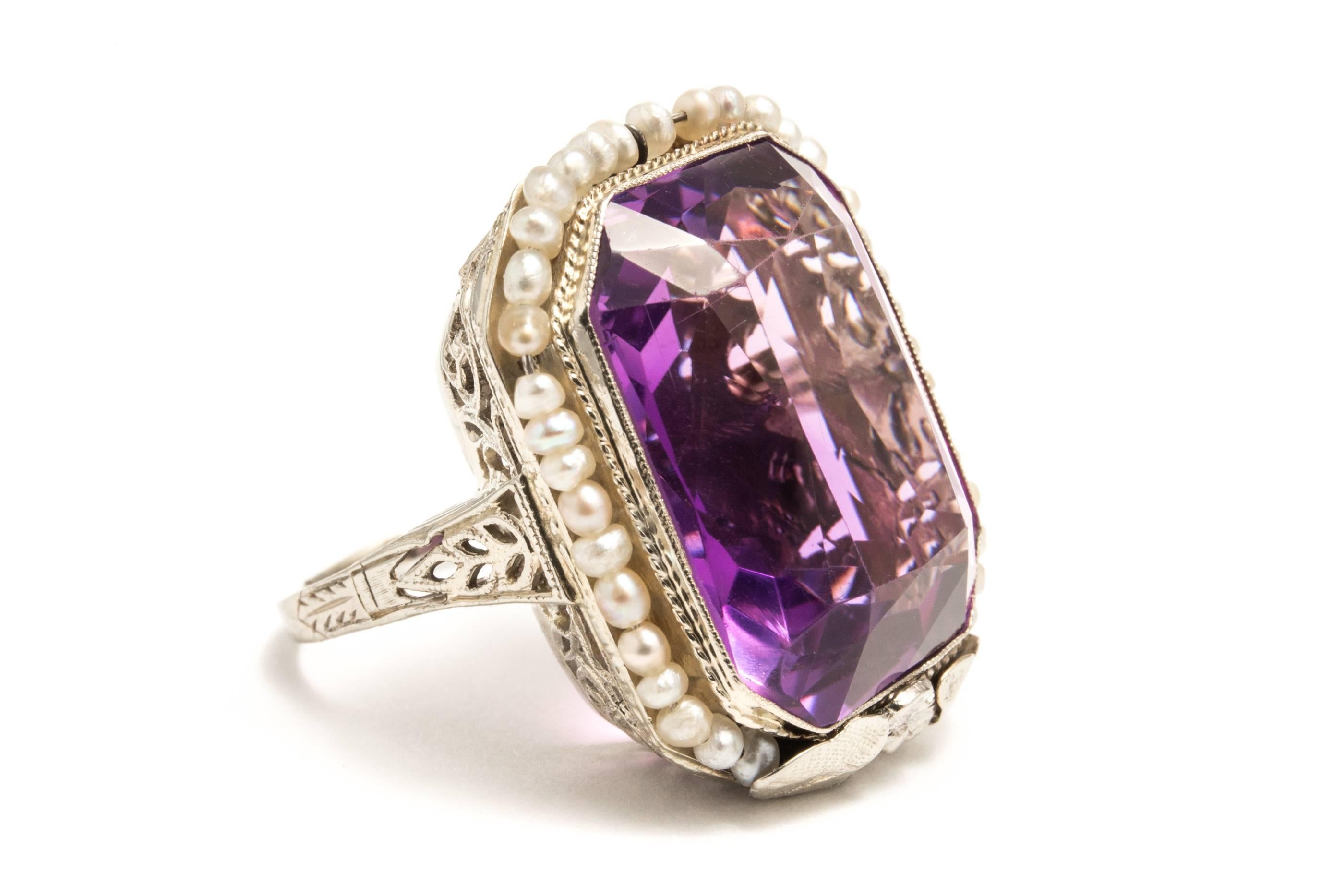 A beautiful original art deco period amethyst and pearl ring in 18 karat white gold.  Centered by a beautiful rectangular shaped amethyst, this ring features a halo of seed pearls surrounding the amethyst.

Weighing approximately 21 carats by