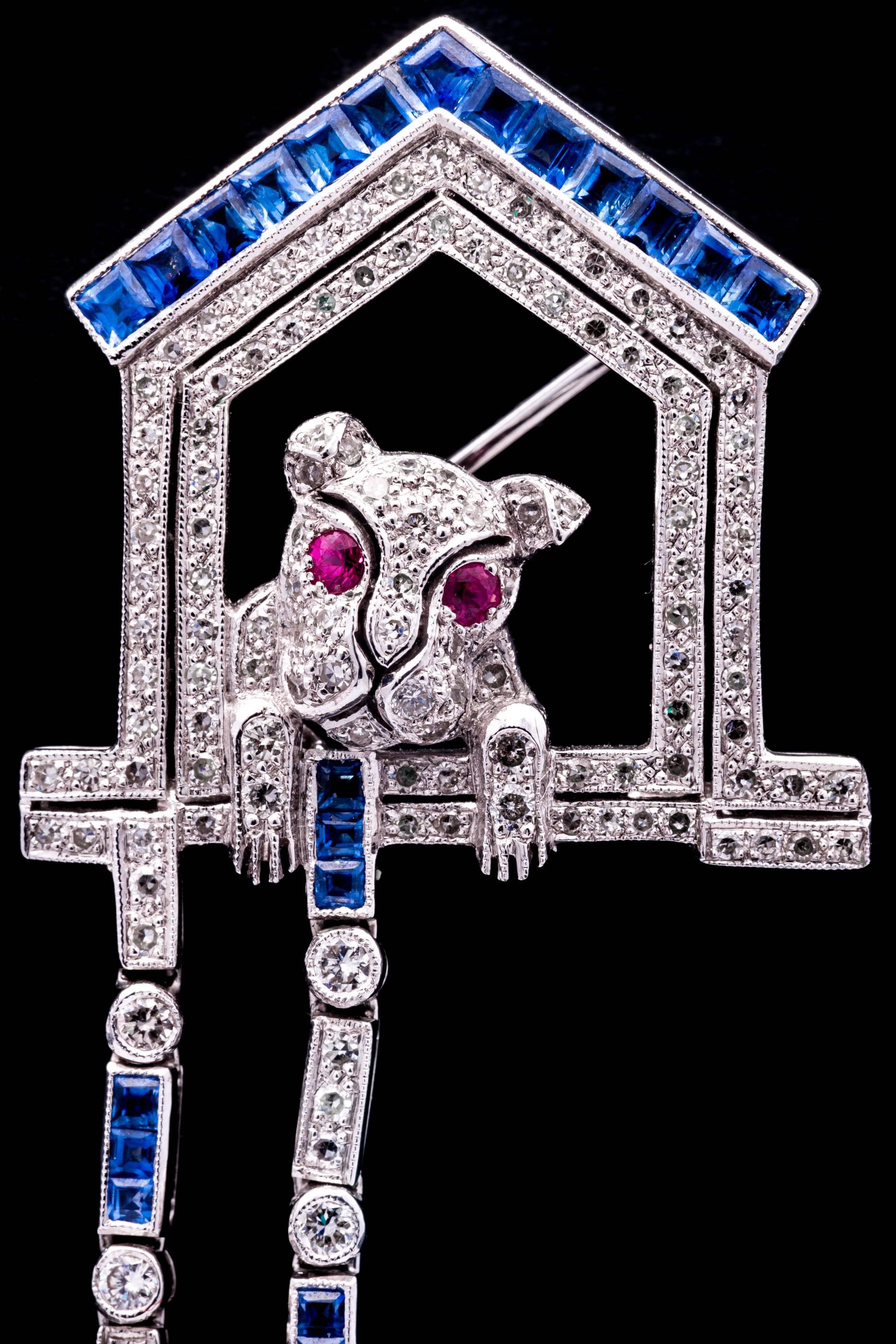 A beautiful handmade and articulated dog in do house brooch with moving leash.  Crafted in 18 karat white gold, this beautiful brooch is pave set throughout with antique Swiss cut diamonds accented by rich blue sapphires and vivid red rubies.

In