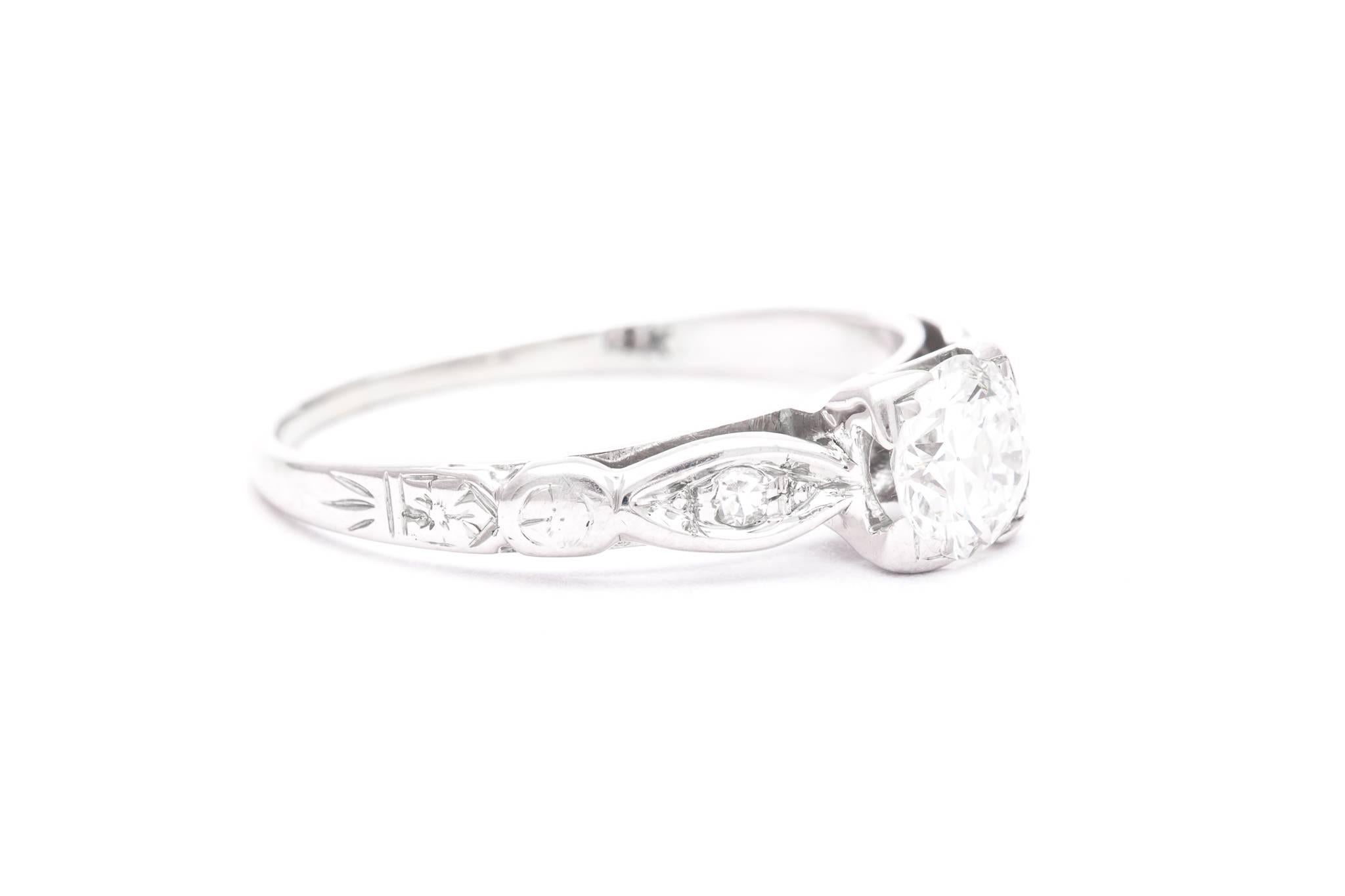A beautiful mid century hand engraved diamond engagement ring in 18 karat white gold.  Centered by a 0.50 carat old European cut diamond this ring features a pair of accenting Swiss cut diamonds on either side of the center diamond giving the ring a