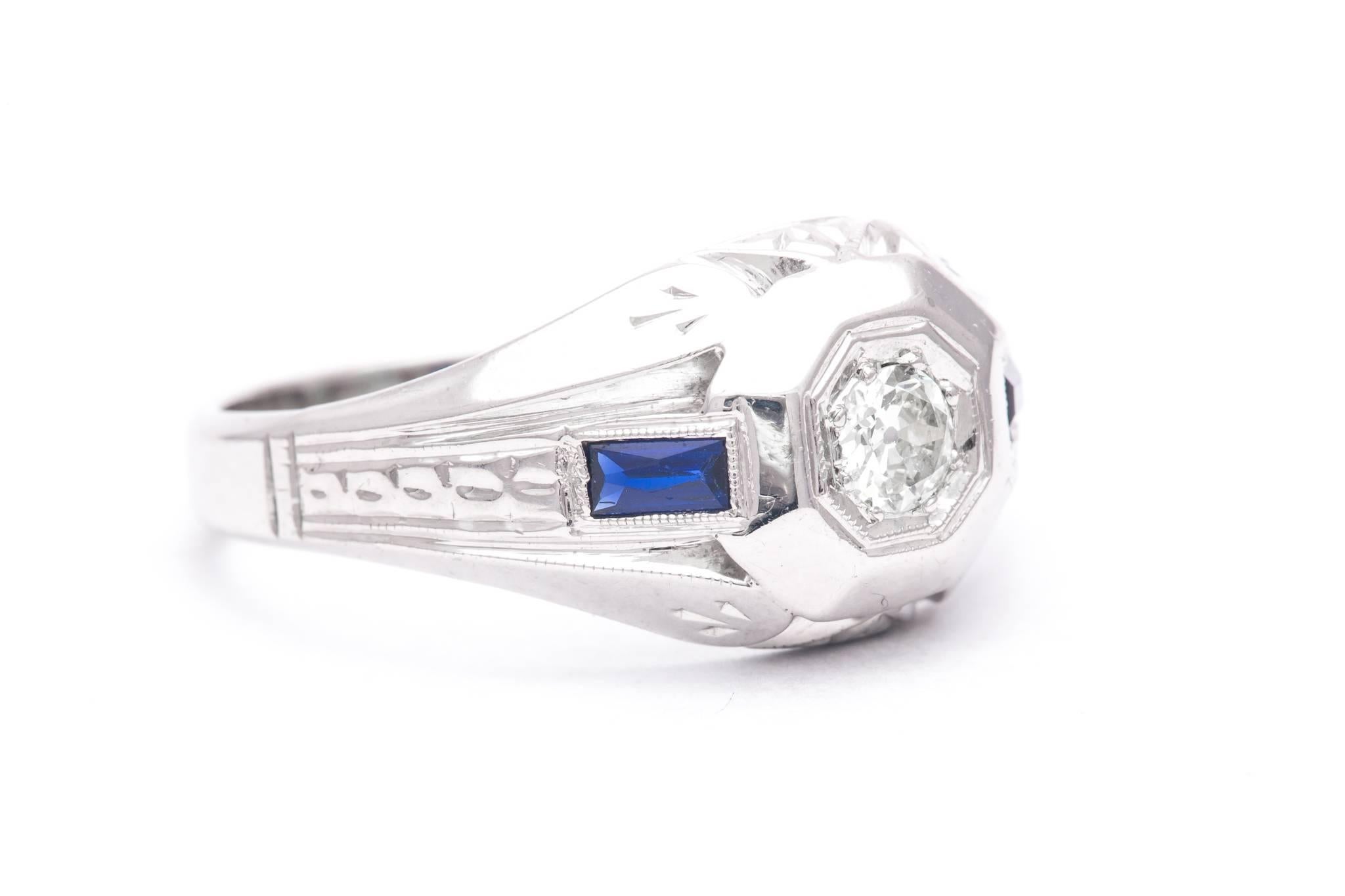 An original art deco period mens diamond, and sapphire ring in 18 karat white gold.  Centered by a sparkling antique mine cut diamond weighing 0.25 carats this ring features a pair of accenting French cut sapphires weighing a combined 0.40
