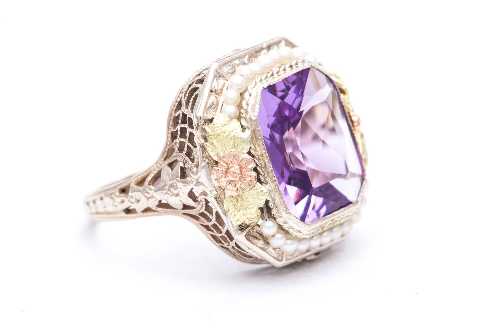 An original art deco period amethyst and pearl ring in try color white, rose, and yellow gold.  Centered by a rectangular high quality rich vivid purple amethyst, this ring features a surrounding halo of seed pearls framed by multi color rose and