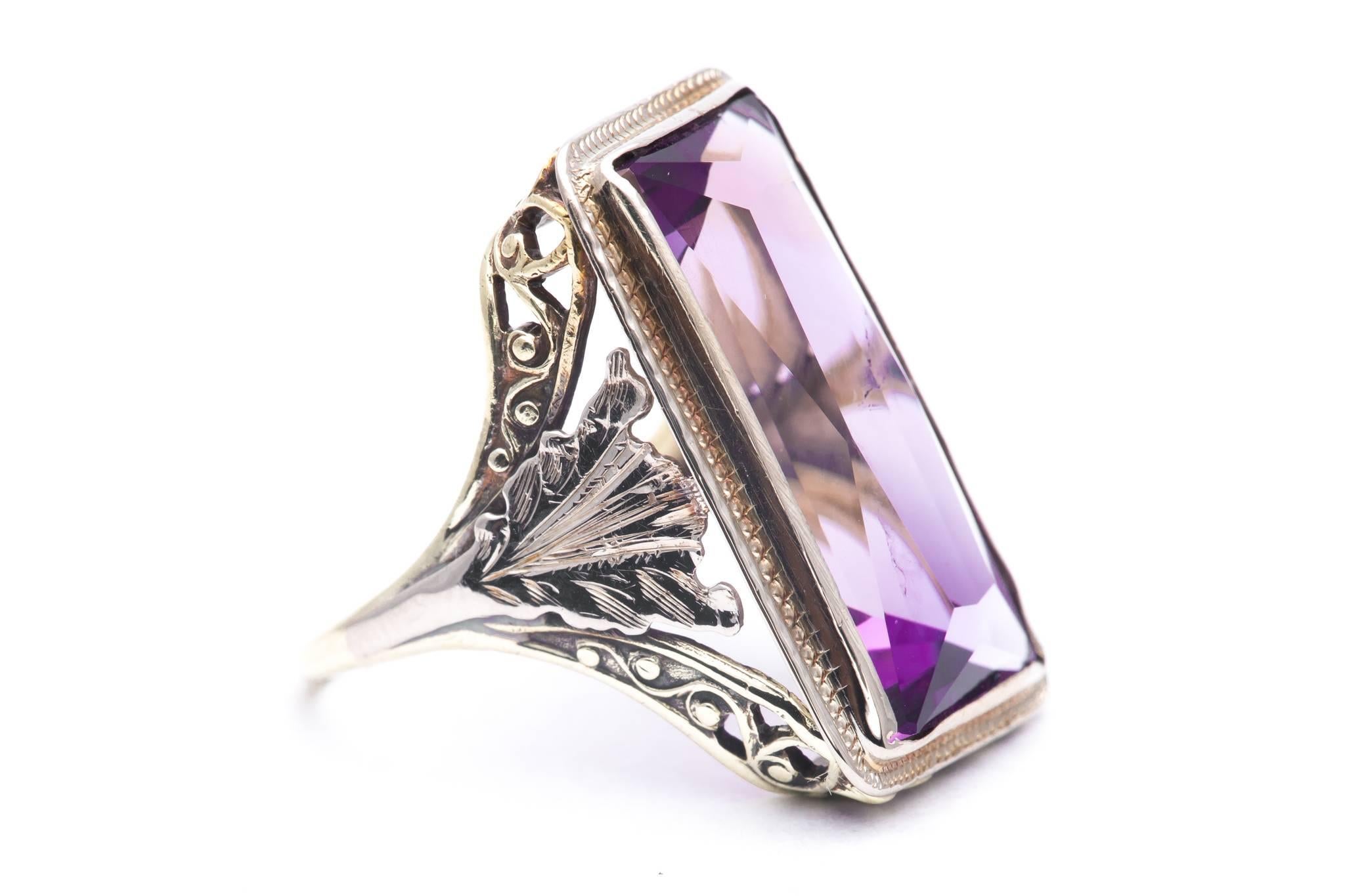 An original art nouveau period amethyst solitaire filigree ring in yellow gold and platinum.  Centered by a sizable rectangular cut amethyst this ring features a two tone platinum and yellow gold mounting with hand formed wire filigree and scroll