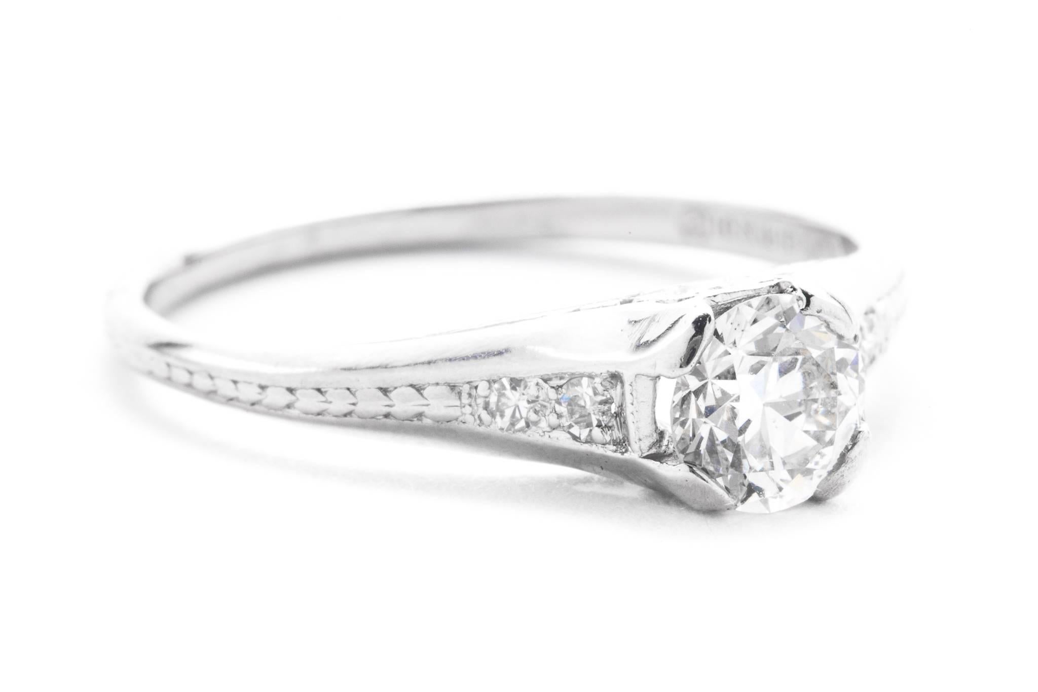 An original art deco period diamond engagement ring in luxurious platinum.  Centered by a 0.70 carat antique European cut diamond this ring features beautiful hand engraving in a traditional art deco manner along with accenting pave set