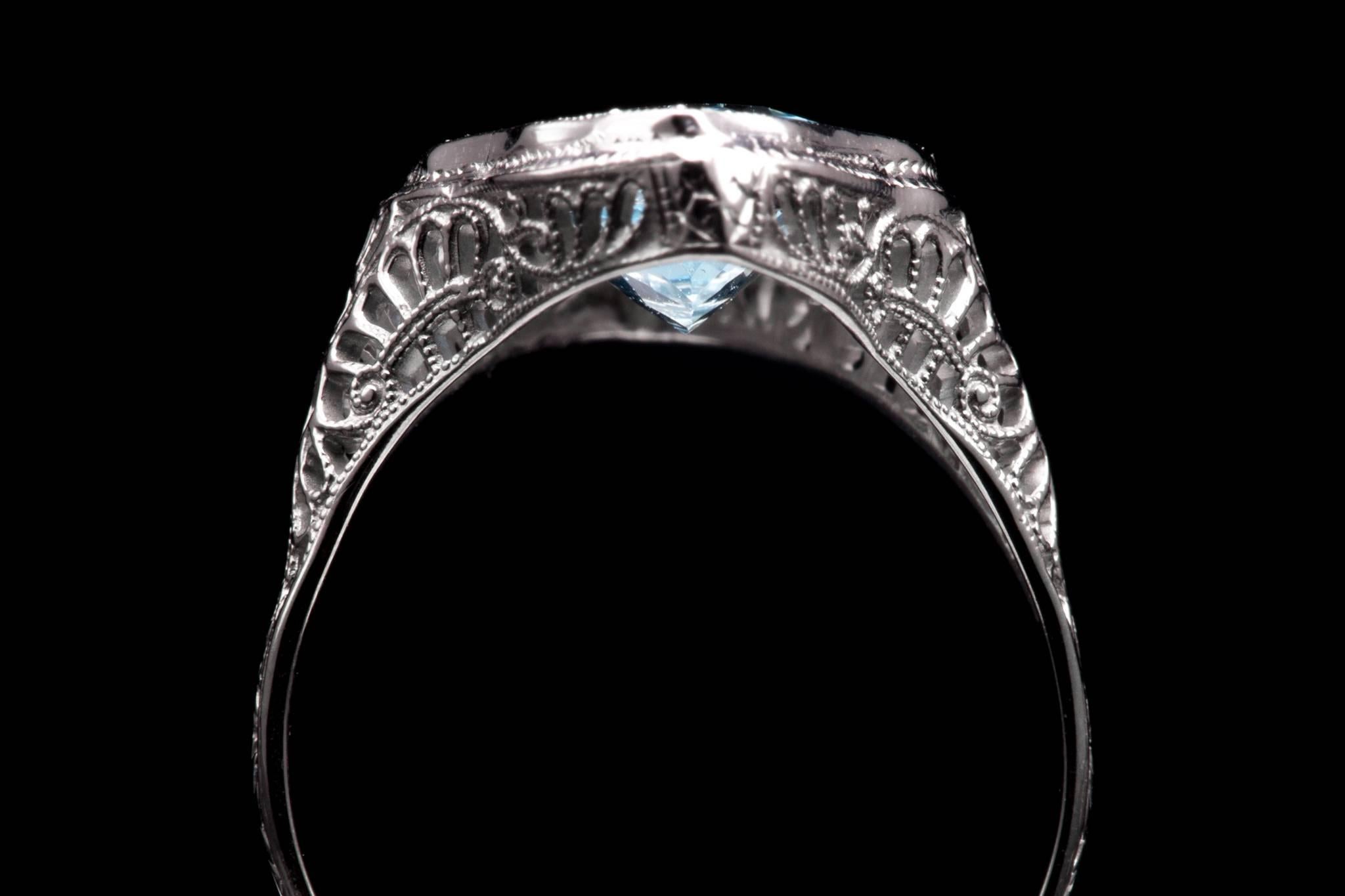 A beautiful art deco period diamond and aquamarine ring in 18 karat white gold.  Featuring hand pierced filigree and milligram detailing throughout this ring is centered by a vivacious aquamarine and a pair of antique European cut