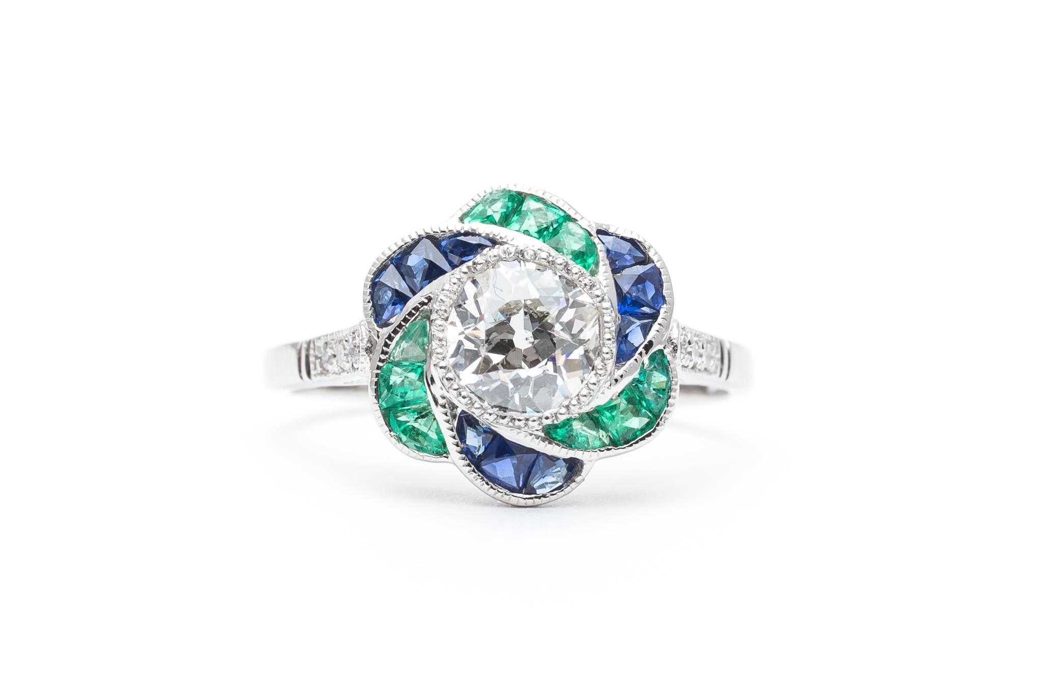 A stunning floral motif diamond, emerald, and sapphire ring crafted in luxurious platinum. Centered by a dazzling 0.75ct old European diamond, this ring features shimmering sapphire and emerald petals surrounding the center diamond.

Bezel set in a