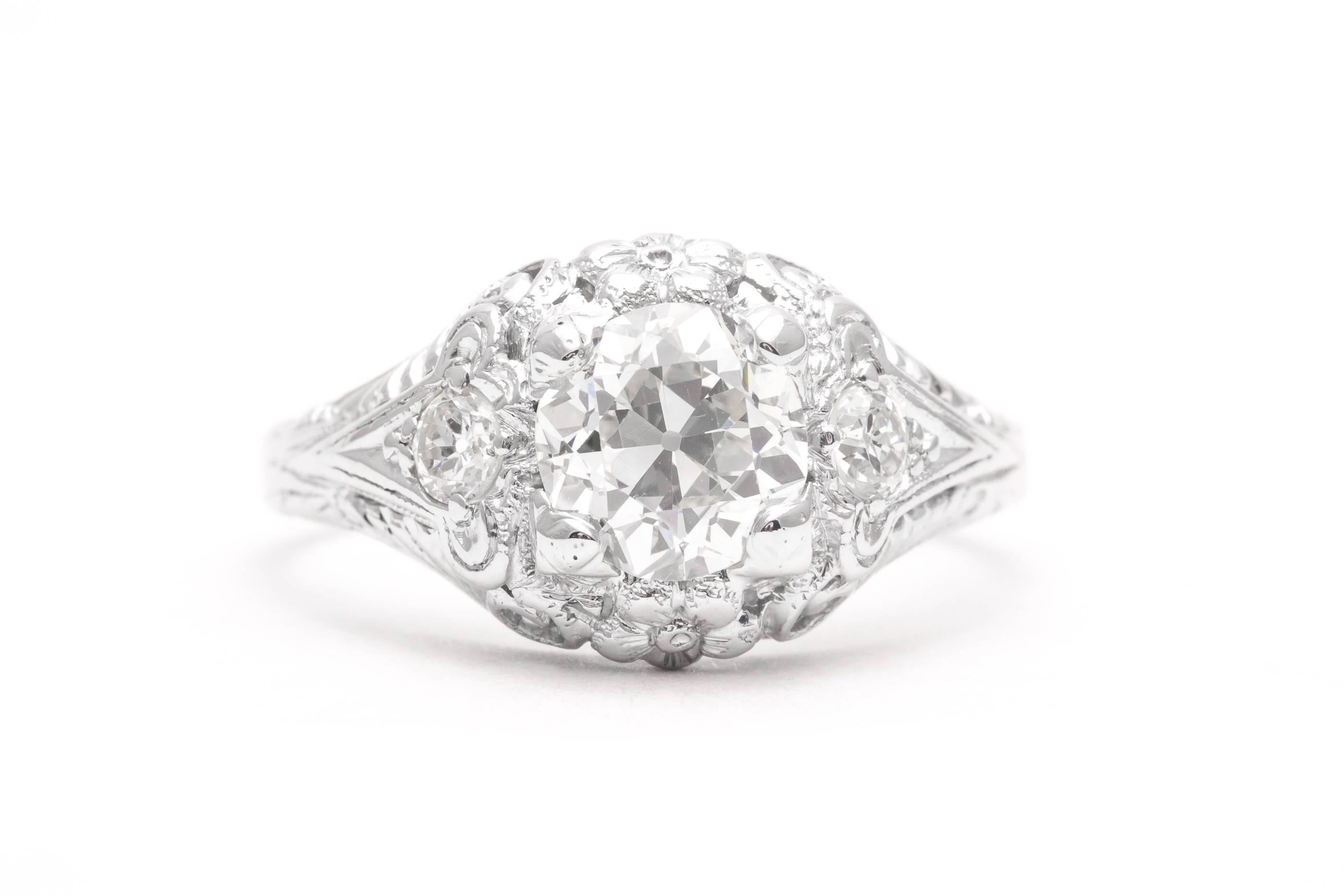 A beautiful art deco period diamond engagement ring in luxurious platinum.  Centered by a trio of old European cut diamonds this ring features beautiful hand pierced filigree work throughout complemented by hand carved flowers making this ring a