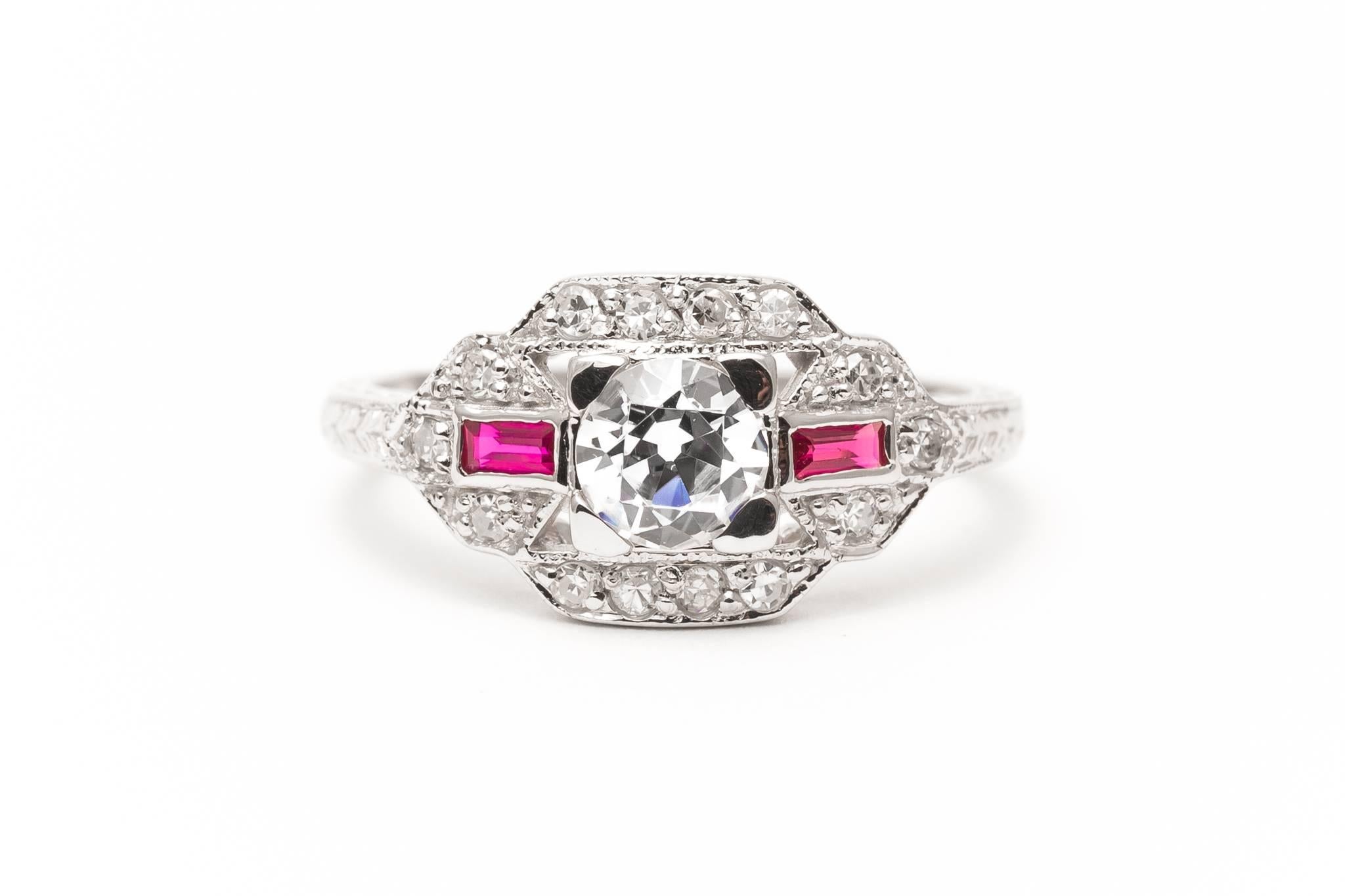 A beautiful hand engraved diamond and ruby ring in 14 karat white gold. Centered by a sparkling antique old European cut diamond of 0.42 carats this ring features antique single cut diamonds set throughout, as well as two baguette cut rubies adding