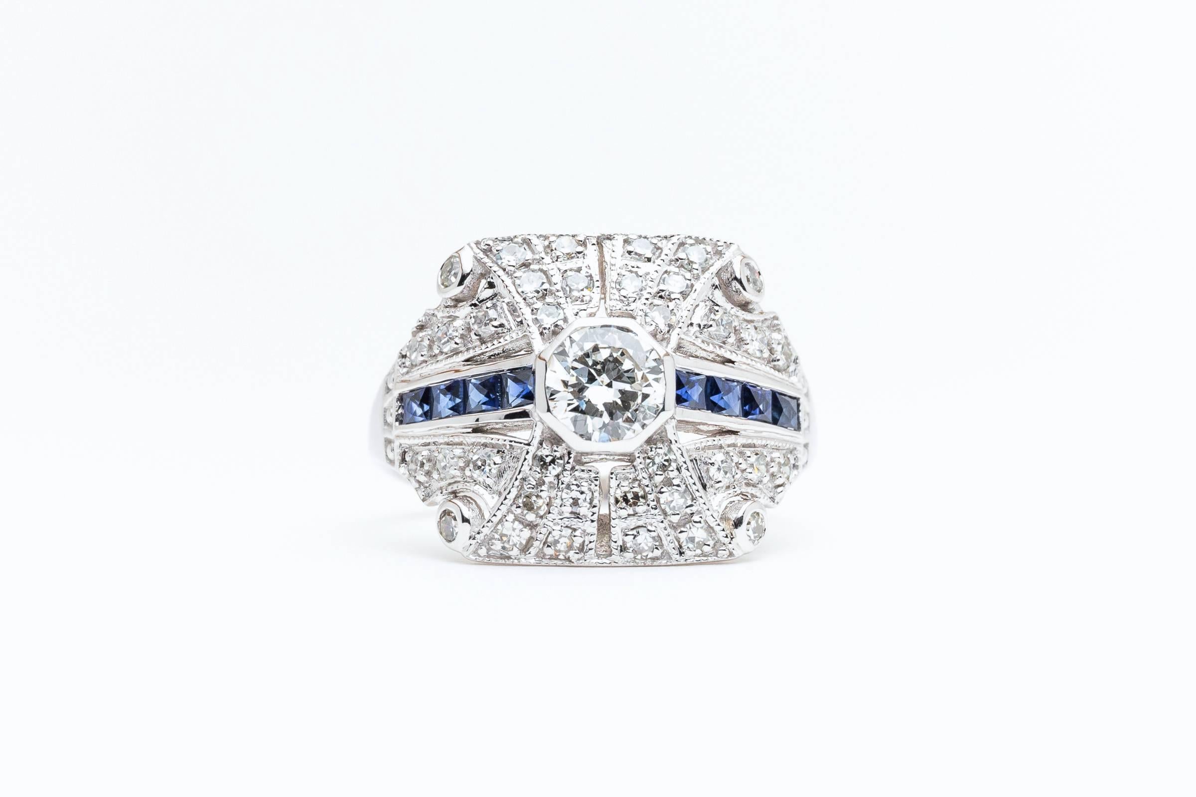 A beautiful diamond and sapphire ring in 14 karat white gold. Featuring a high quality European cut diamond weighing 0.50 carats, this beautiful ring features rich blue French cut sapphires and accenting diamonds in a hand crafted 14 karat white