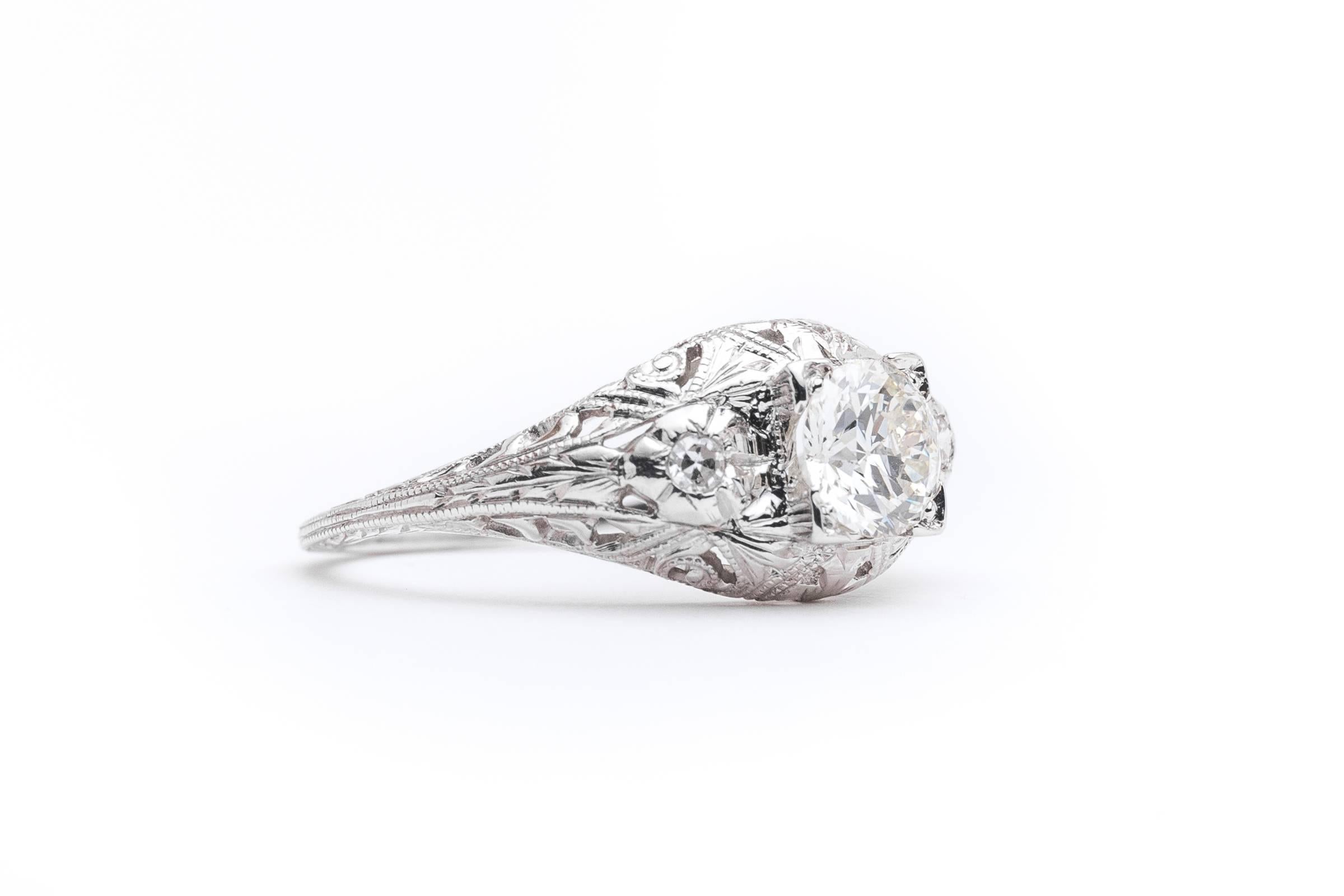 A beautiful art deco period diamond engagement ring in luxurious platinum. Featuring beautiful hand pierced filigree work and floral motif engraving throughout this engagement ring is centered by a beautiful old European cut diamond framed by a pair