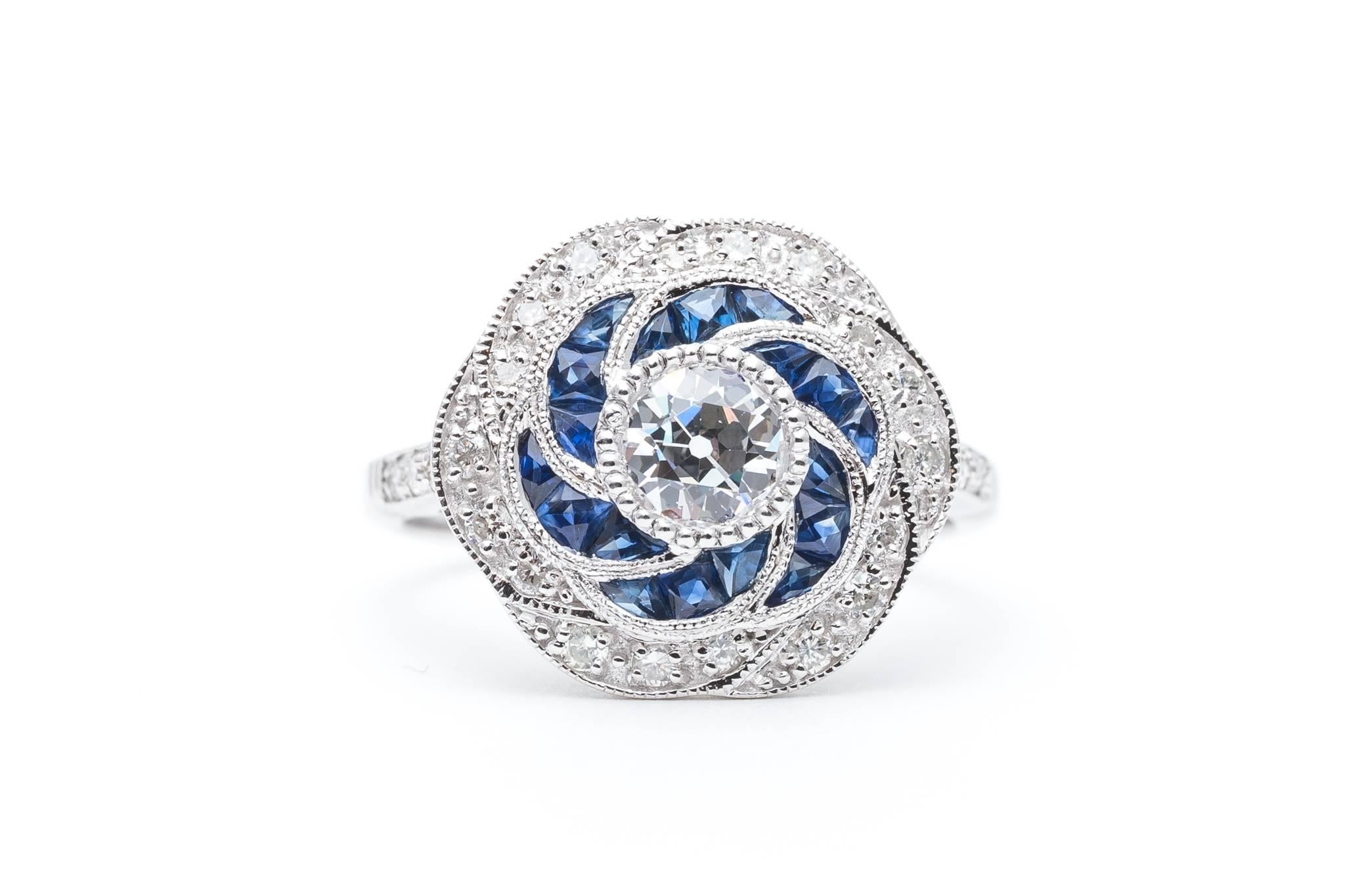 Beacon Hill Jewelers Presents:

A beautiful vintage floral inspired diamond and sapphire engagement ring in 14 karat white gold. Centered by a sparkling bezel set old European cut diamond this ring features flower petals of French cut sapphires