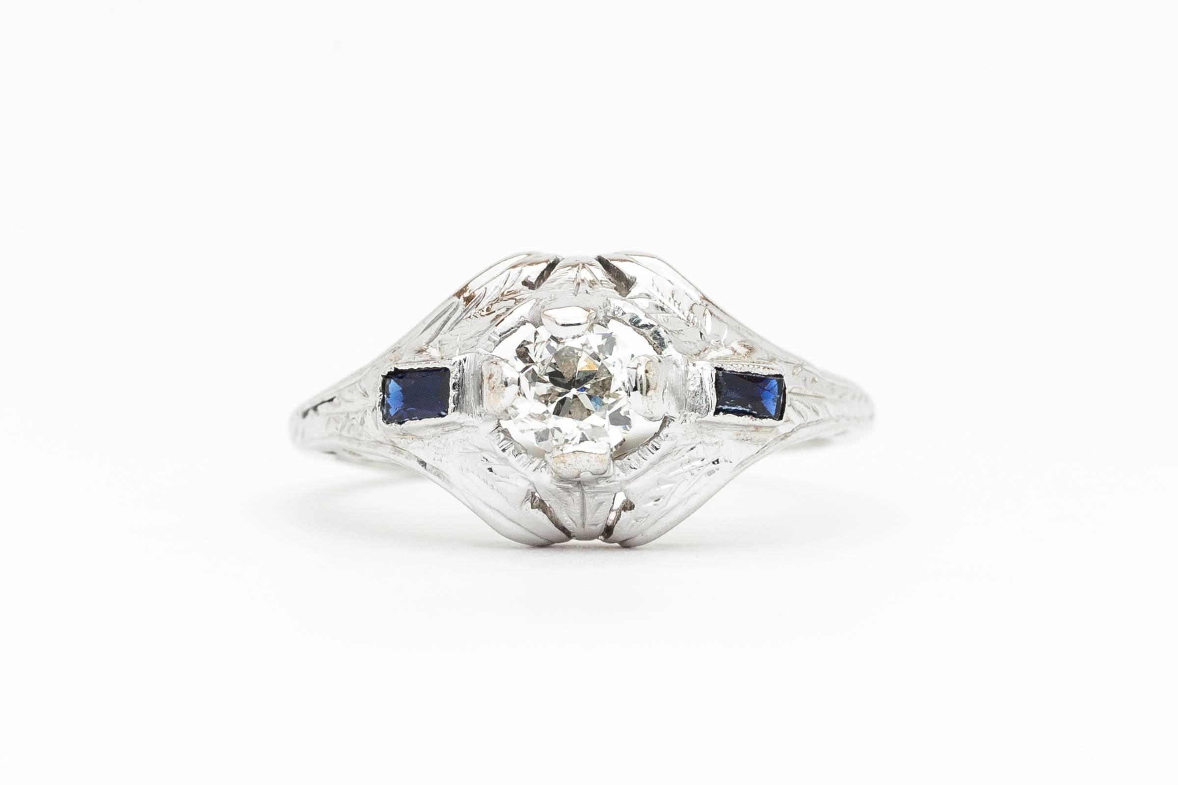 Beacon Hill Jewelers Presents:

A beautiful art deco period diamond and sapphire engagement ring in 18 karat white gold. Centered by a sparkling 0.40ct old European cut diamond this ring features beautiful hand engraving and filigree work
