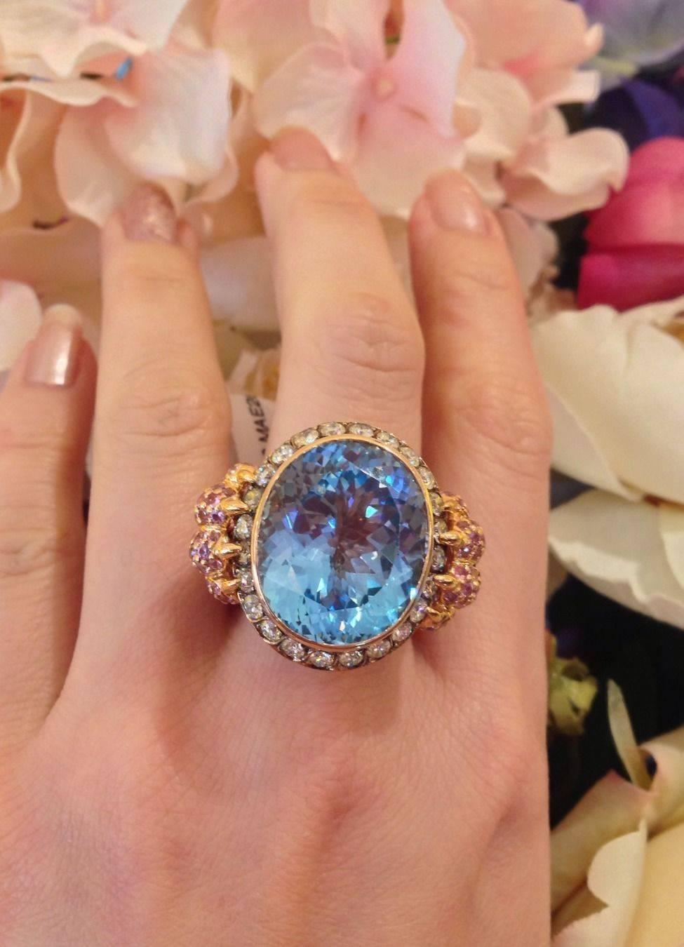 Center stone is Oval Blue Topaz 32.82 ct bezel set, surrounded by 23 round brilliant diamonds weighing 1.63 ct total, VS-SI clarity, I-J color.
Ring contains 3.01 ct of Pink, Yellow and Blue Sapphires, pave set along shank and gallery and sides. 