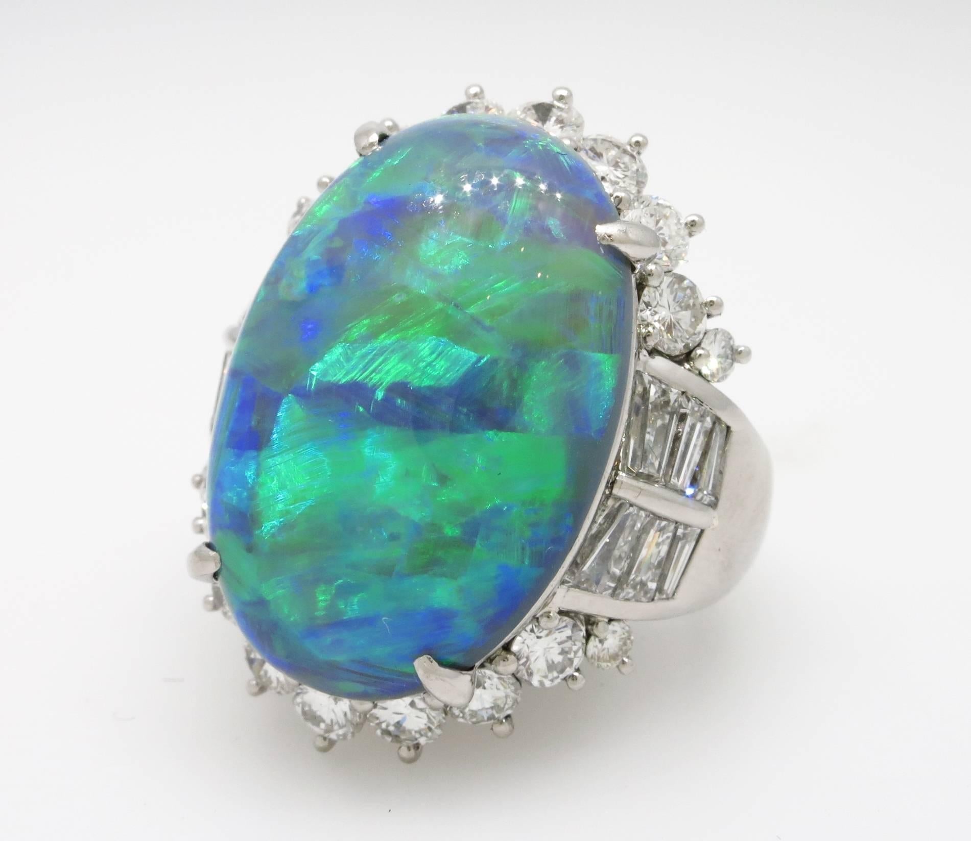 Ring features a beautiful 14.91 ct oval shaped black opal cabochon in the center with flashes of green, yellow, and blue, with dark grey background, surrounded by 3.11 cts of round and baguette diamonds, H color and VS-SI1 clarity.  Set in Platinum.