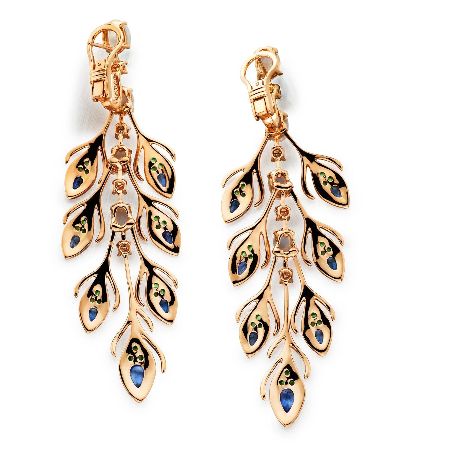 The Peacock’s rain dance when it spreads it’s feathers is one of the most eye catching scenes. These 18k rose gold peacock style dangle earrings are sure to draw attention. Featuring a beautiful combination of green garnet, blue sapphire, moonstone