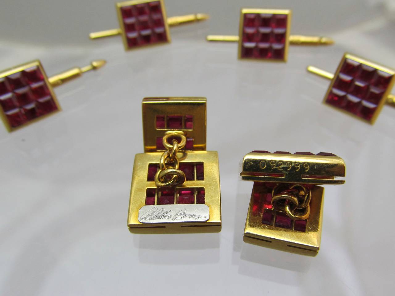 Unique invisibly set style  ruby dress set by Aletto Bros., designed as  a calibre-cut ruby square shaped 4 raw plaques with matching 4 shirt studs.

Estimated total weight of ruby is 18 carats.
18k gold. 
With it's original box
Maker's