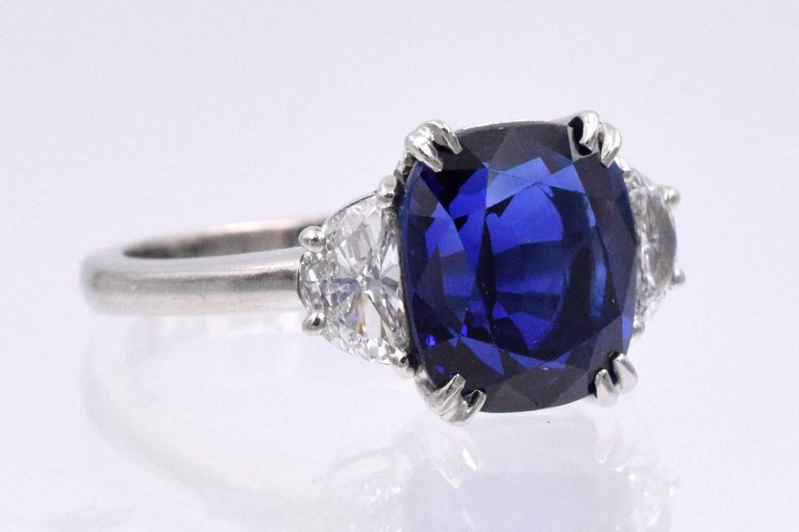 Royal blue, cushion shape  sapphire  flanked by 2 half moon diamonds solitaire ring.
Size of the sapphire is 5.06 carat and 2 half moon diamonds are 0.5 carat( E color VS clarity)
Platinum, 
Ring size is 5.3/4 ( resizable)